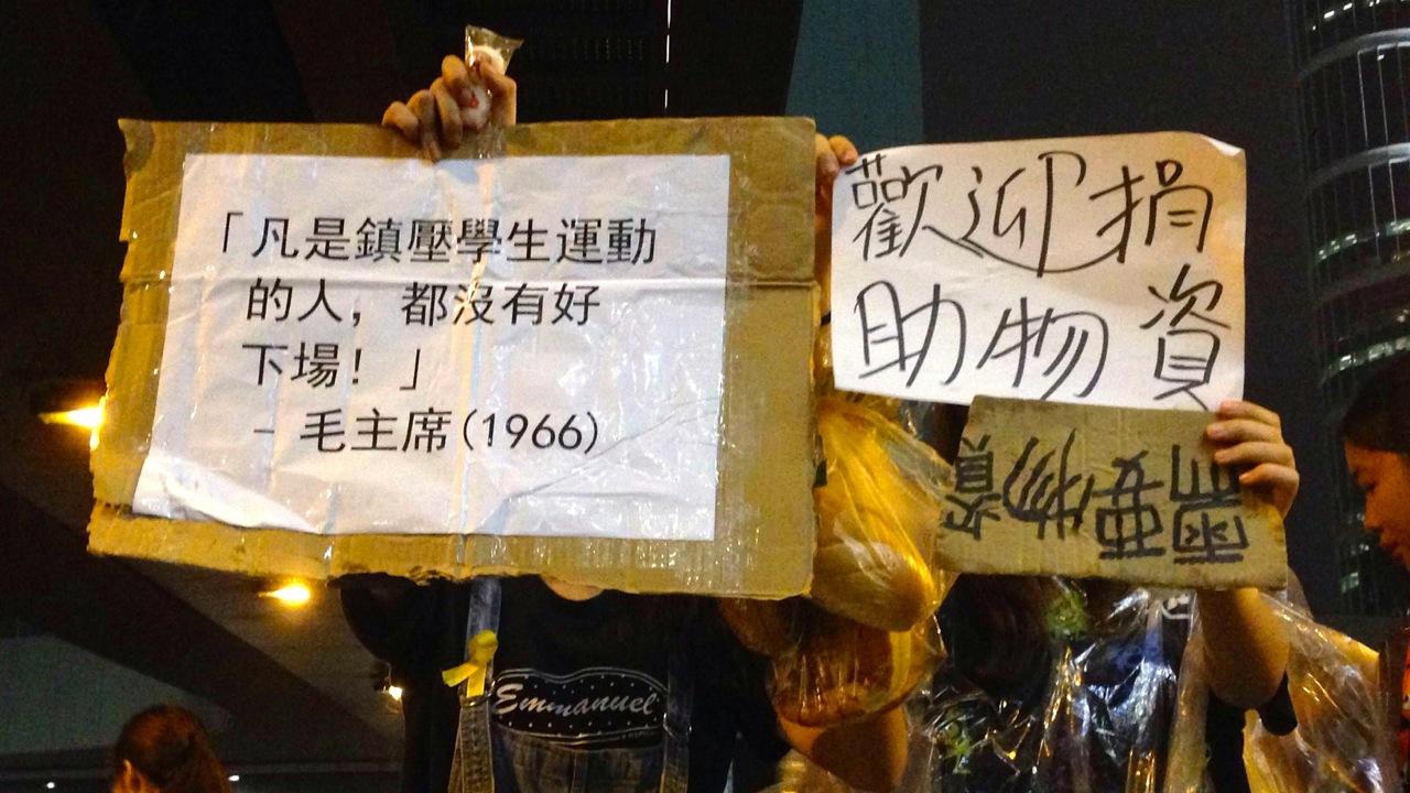 A 19-year-old named Miko (left) held a sign in front of her face because she didn't want to risk having her parents see her at tonight’s protest. Her sign quotes Mao Zedong during the Cultural Revolution: “Those who oppose the student movement will burn i