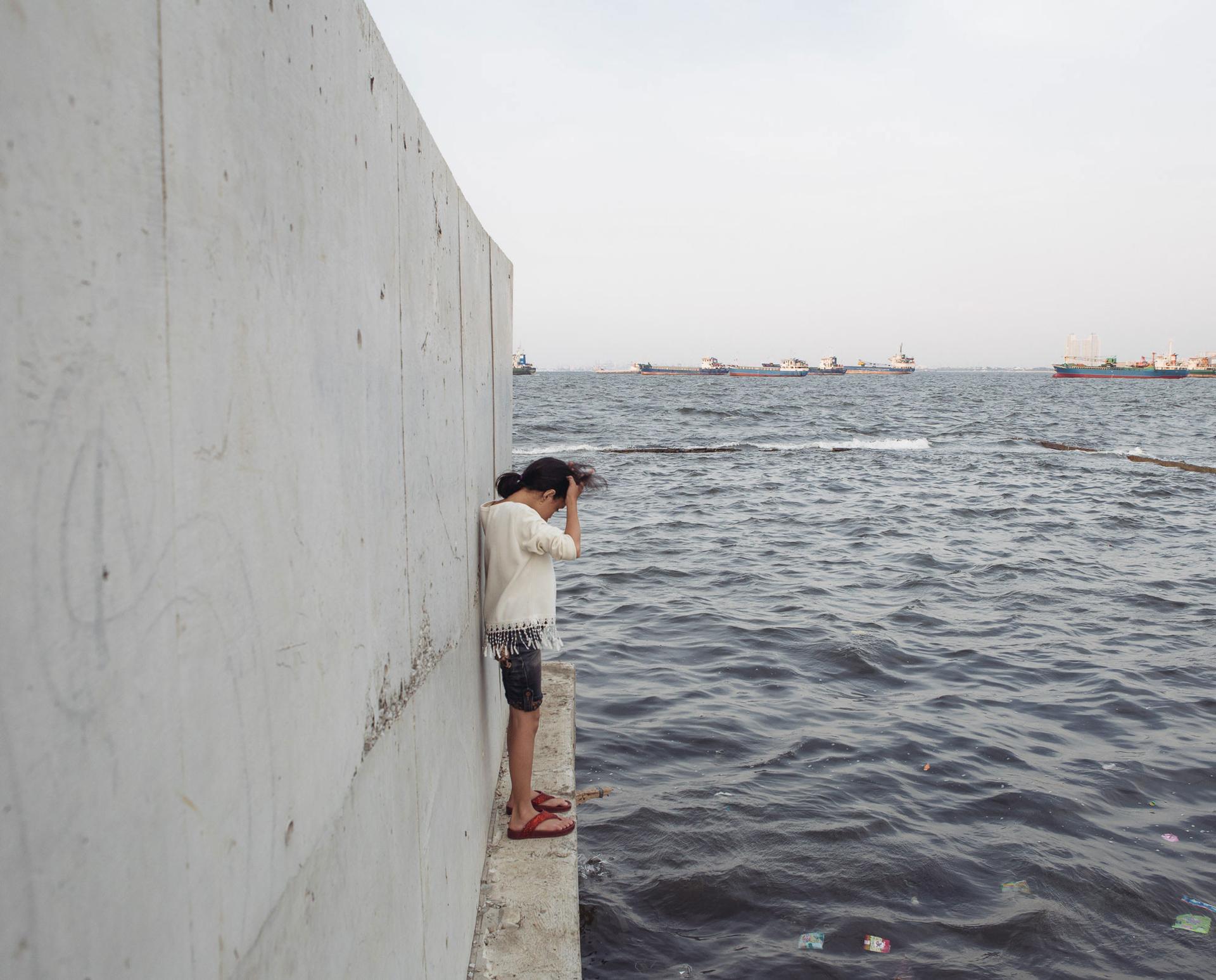 A girl stands on the outer side of a recently reinforced seawall in Muara Baru, Jakarta. The neighborhood on the other side of the wall is below sea level.