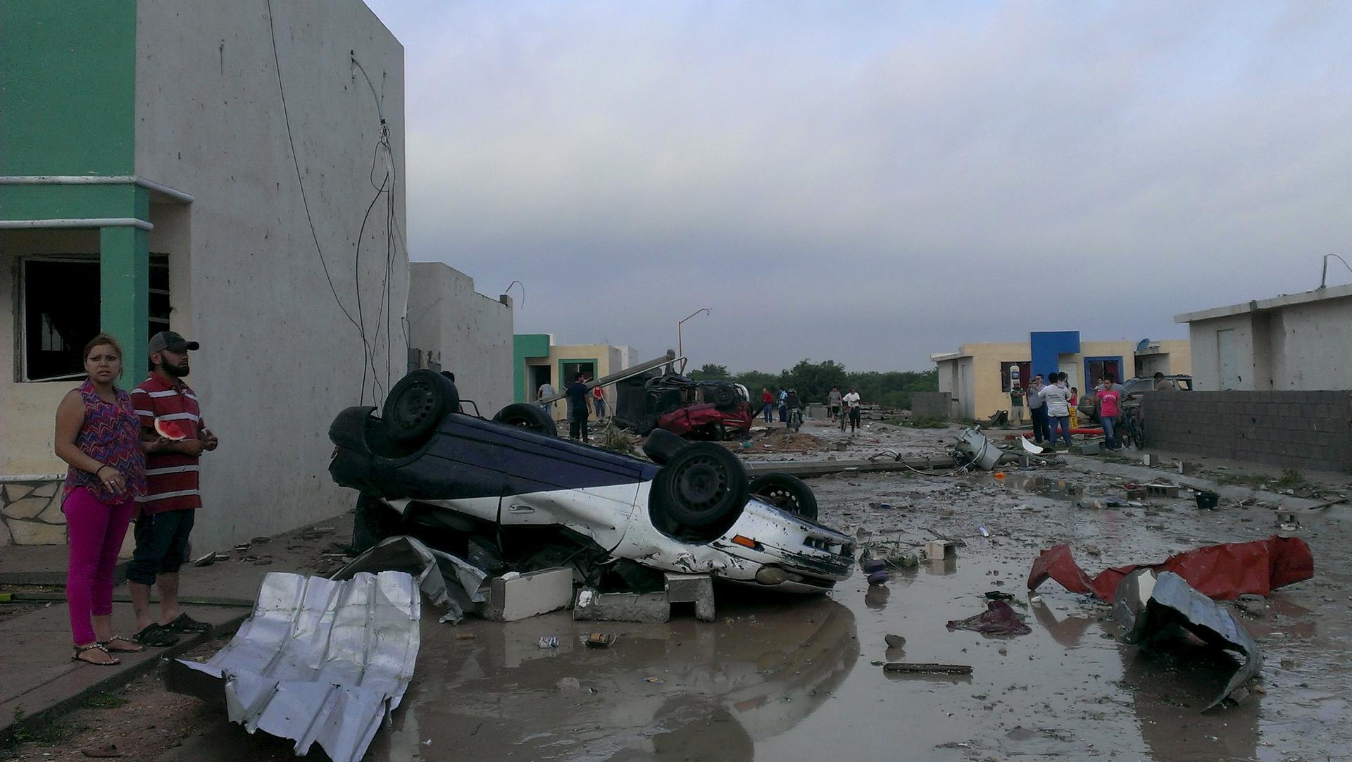 Residents stand next to a damaged car after the tornado hit Ciudad Acuña.