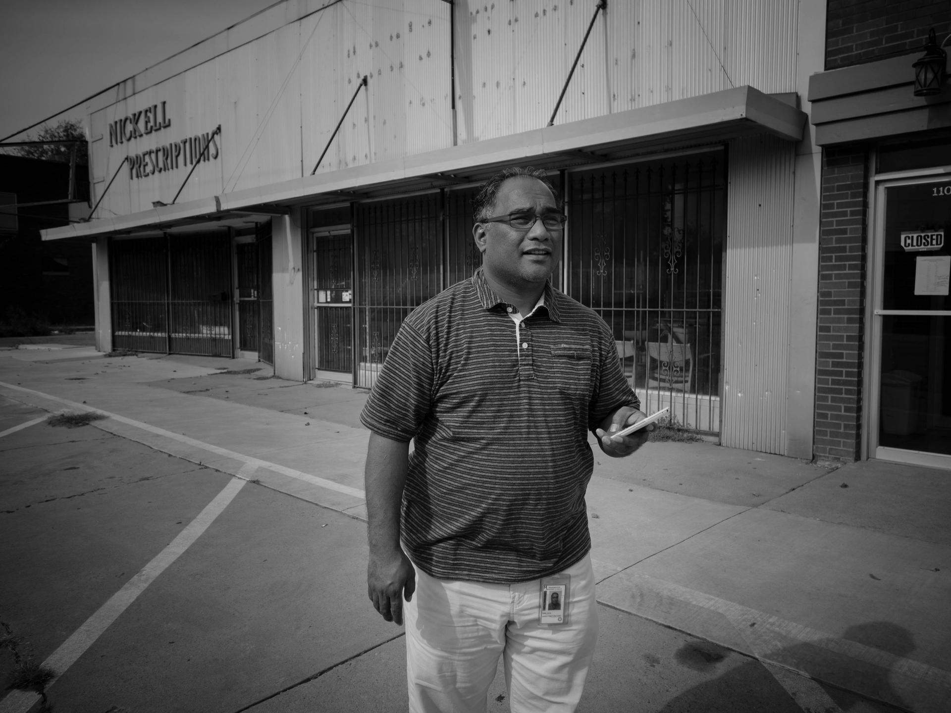 black and white photo of man in front of closed pharmacy