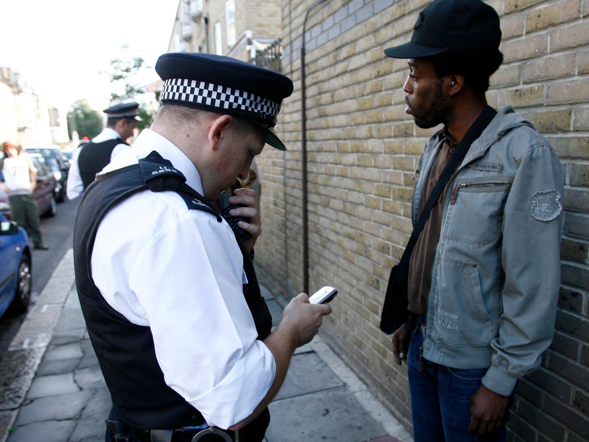 A police officer checks an man's mobile phone after stopping and searching him on a back street in the Brixton neighbourhood of London.