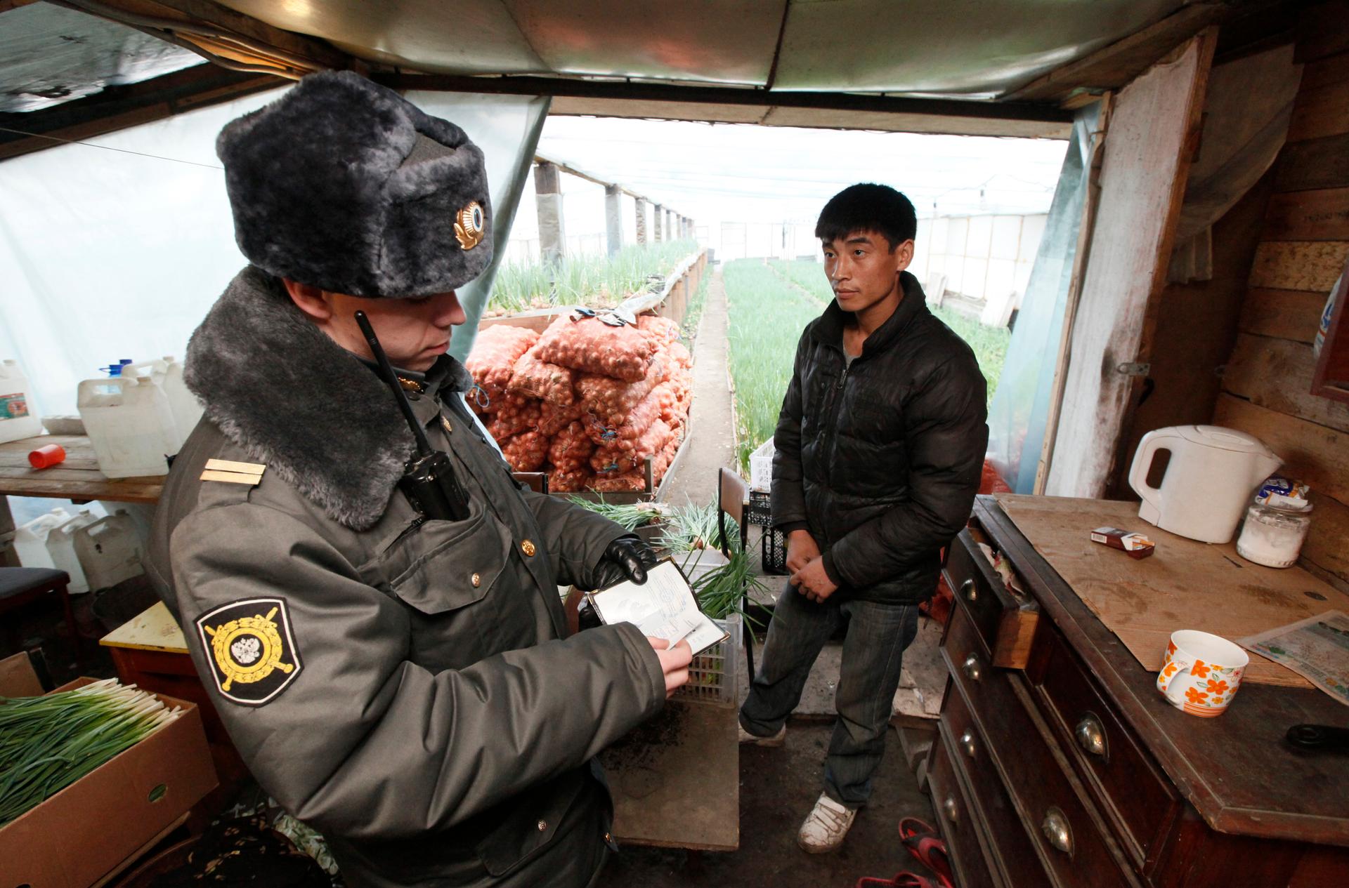 A Russian police officer checks the documents of a Kyrgyz migrant worker at a greenhouse on an agrarian farm during a raid conducted by the police and members of the federal migratory service. April 8, 2012.