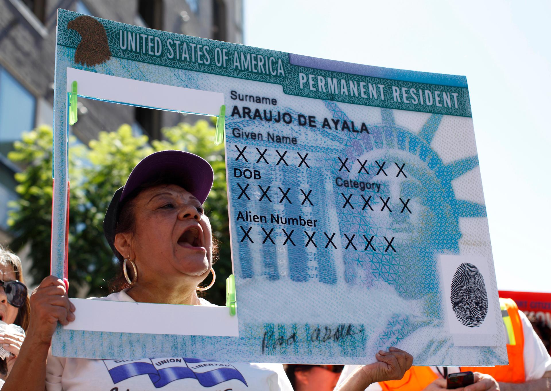 A woman holds a replica green card sign during a protest march to demand immigration reform in Los Angeles, California, Oct. 5, 2013.