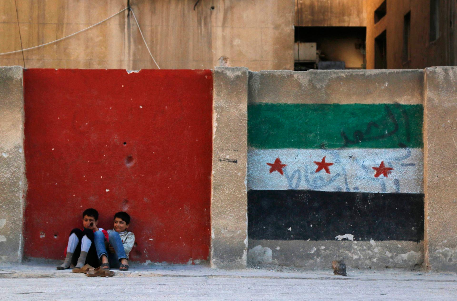 Children sit next to a wall painted with an opposition flag along a street in Aleppo on November 8, 2014.