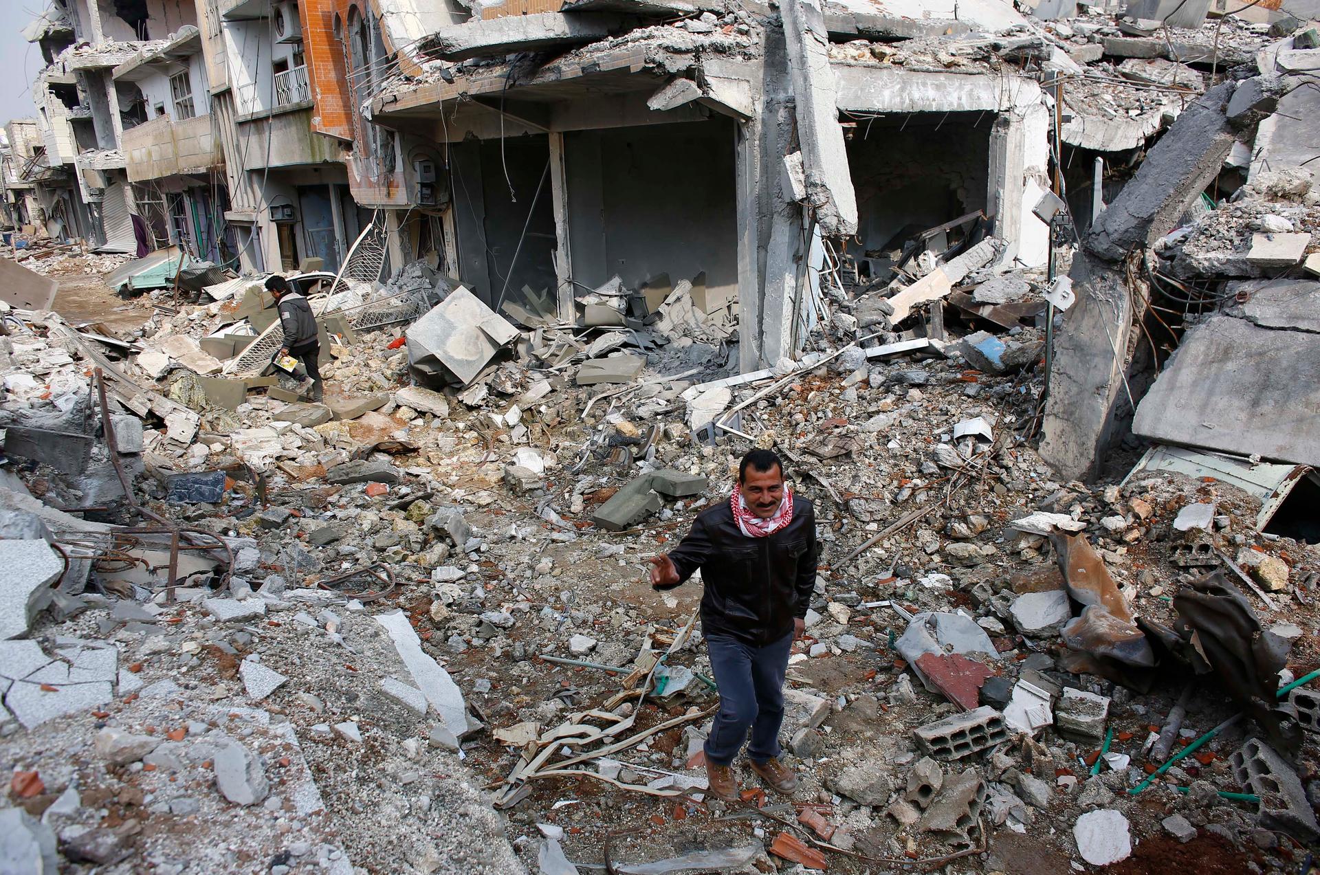 Kurdish men walk on the debris of damaged buildings in the northern Syrian town of Kobane on January 28, 2015.