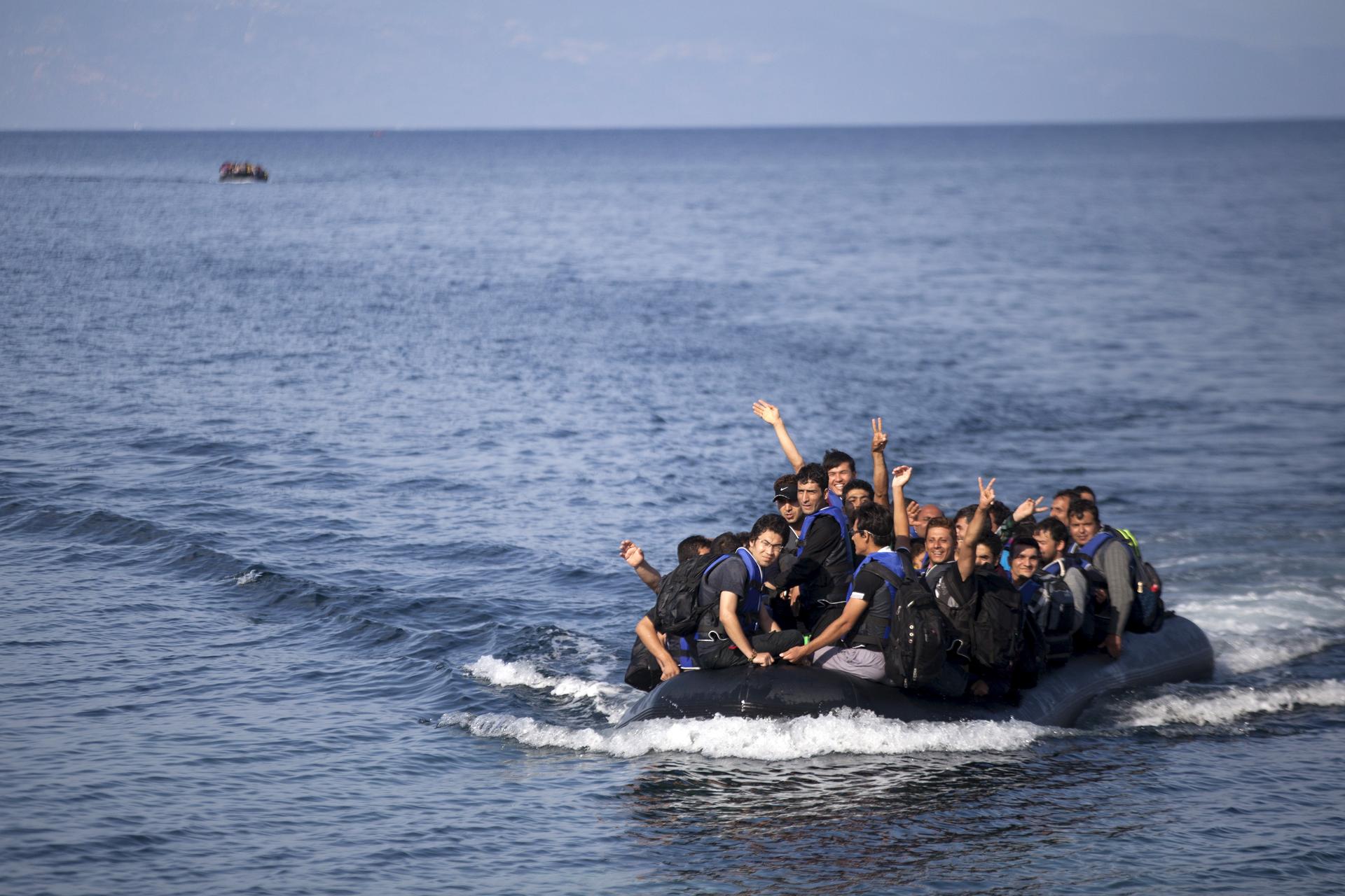 Refugees and migrants on a dinghy wave as they approach the shores of the Greek island of Lesbos.