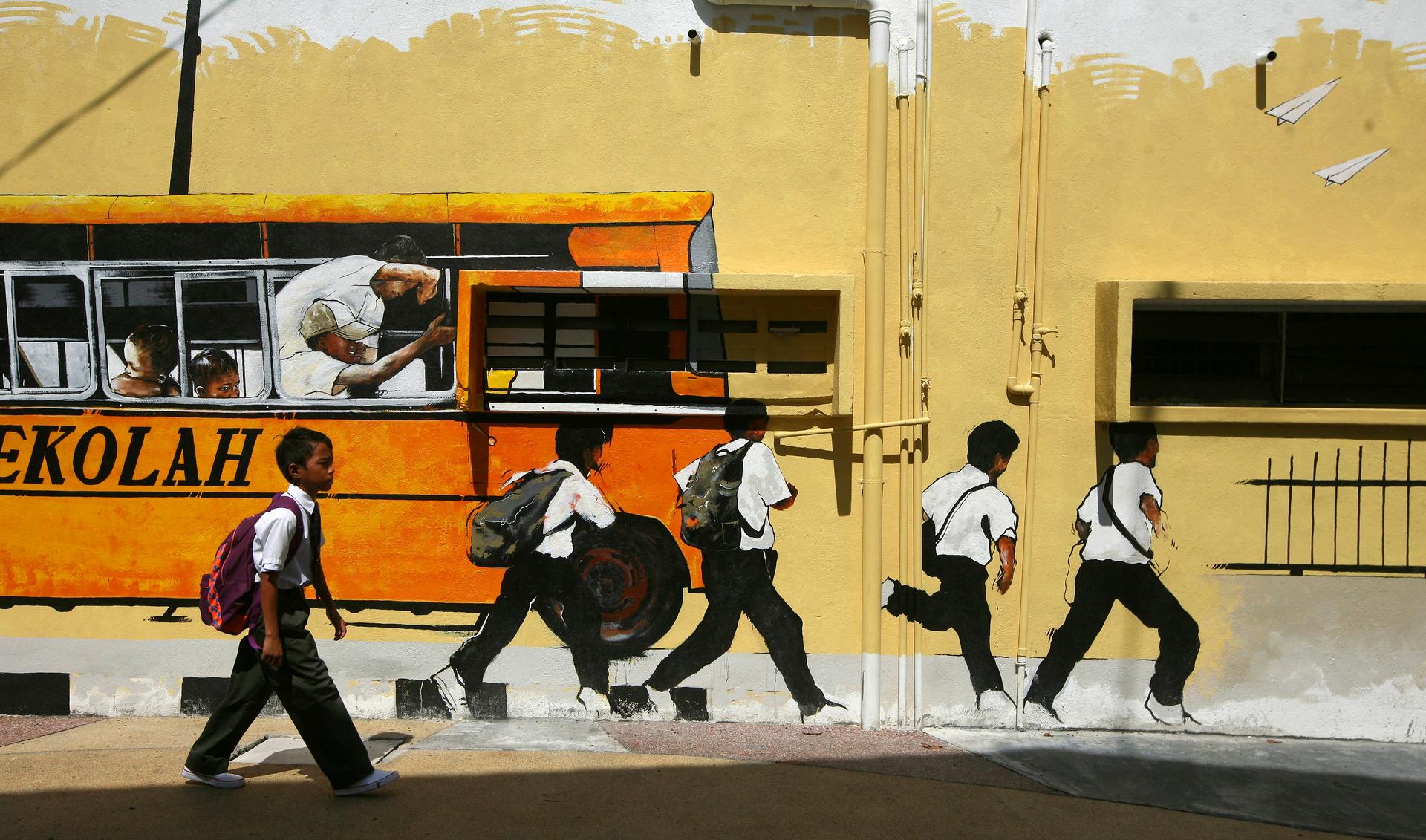 A Malaysian school boy walks past a street mural depicting a school bus and students.
