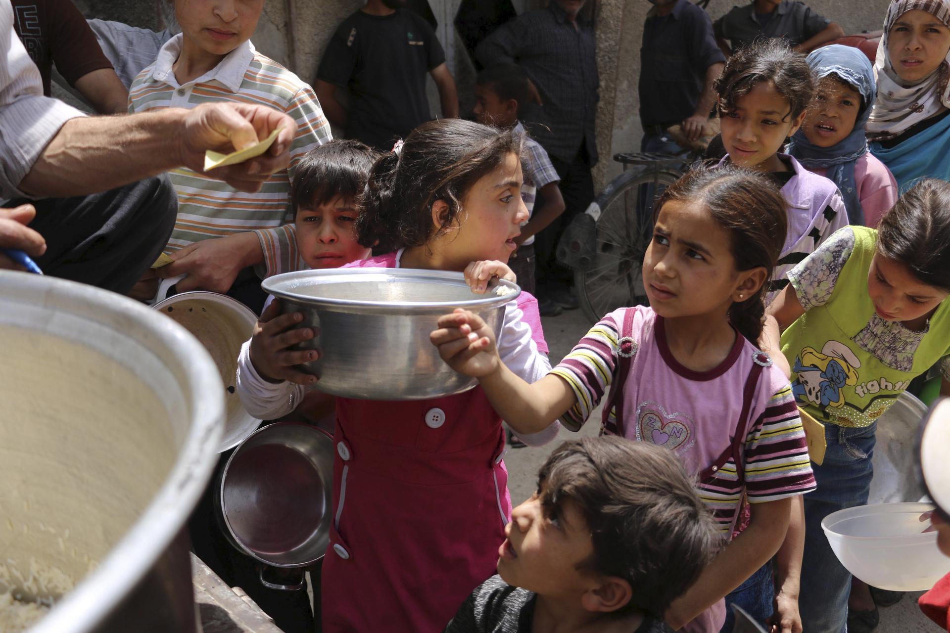 Children carry containers as they queue to receive free meals from a soup kitchen in the besieged town of Deir al-Asafir in the Eastern Ghouta of Damascus May 19, 2015.