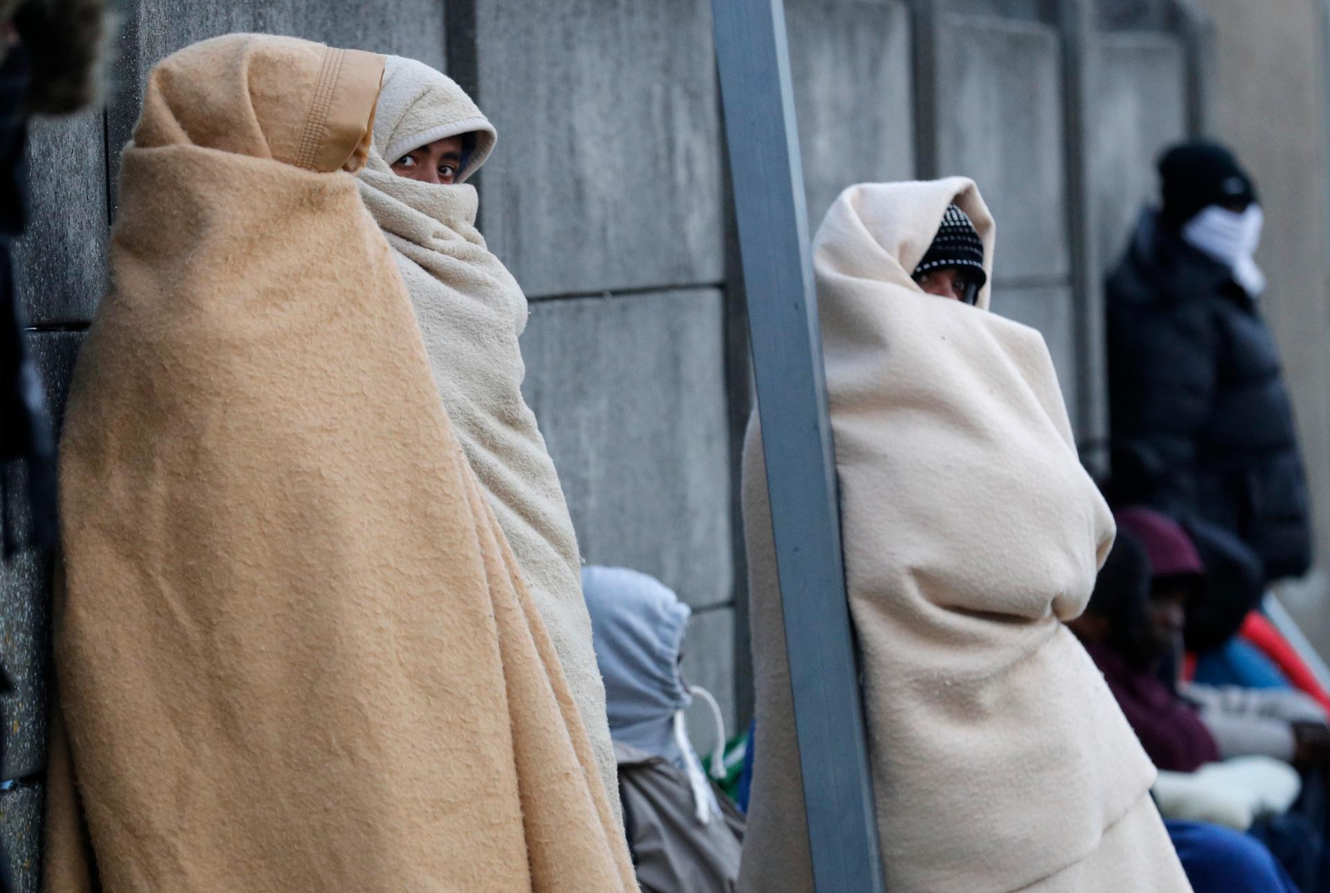 Migrants claiming to be minors use blankets to protect themselves from the cold as they prepare to spend the night on the street after the dismantlement of the 