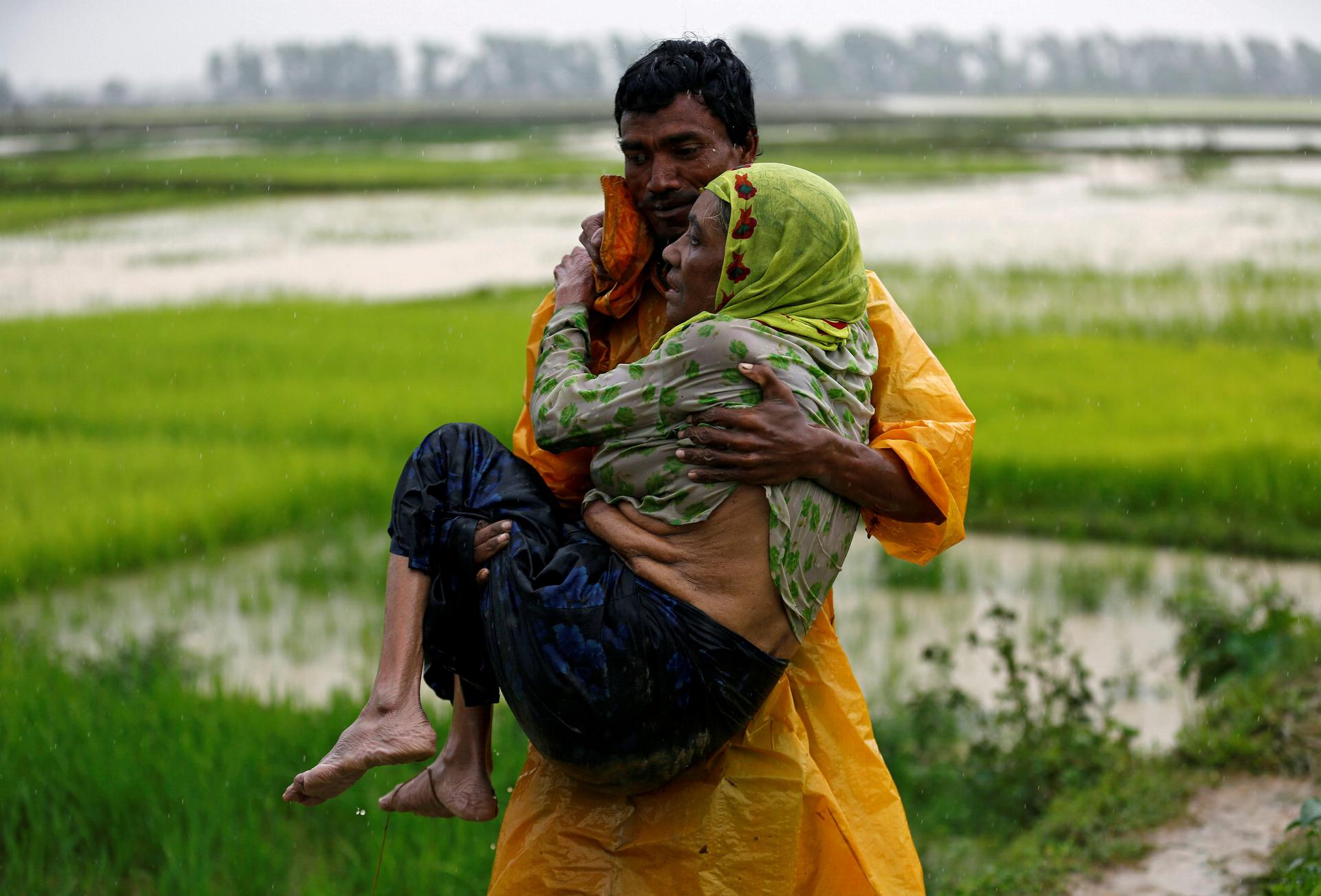 A local man in Teknaf, Bangladesh, carries an elderly Rohingya refugee woman as she is unable to walk after crossing the border from Myanmar
