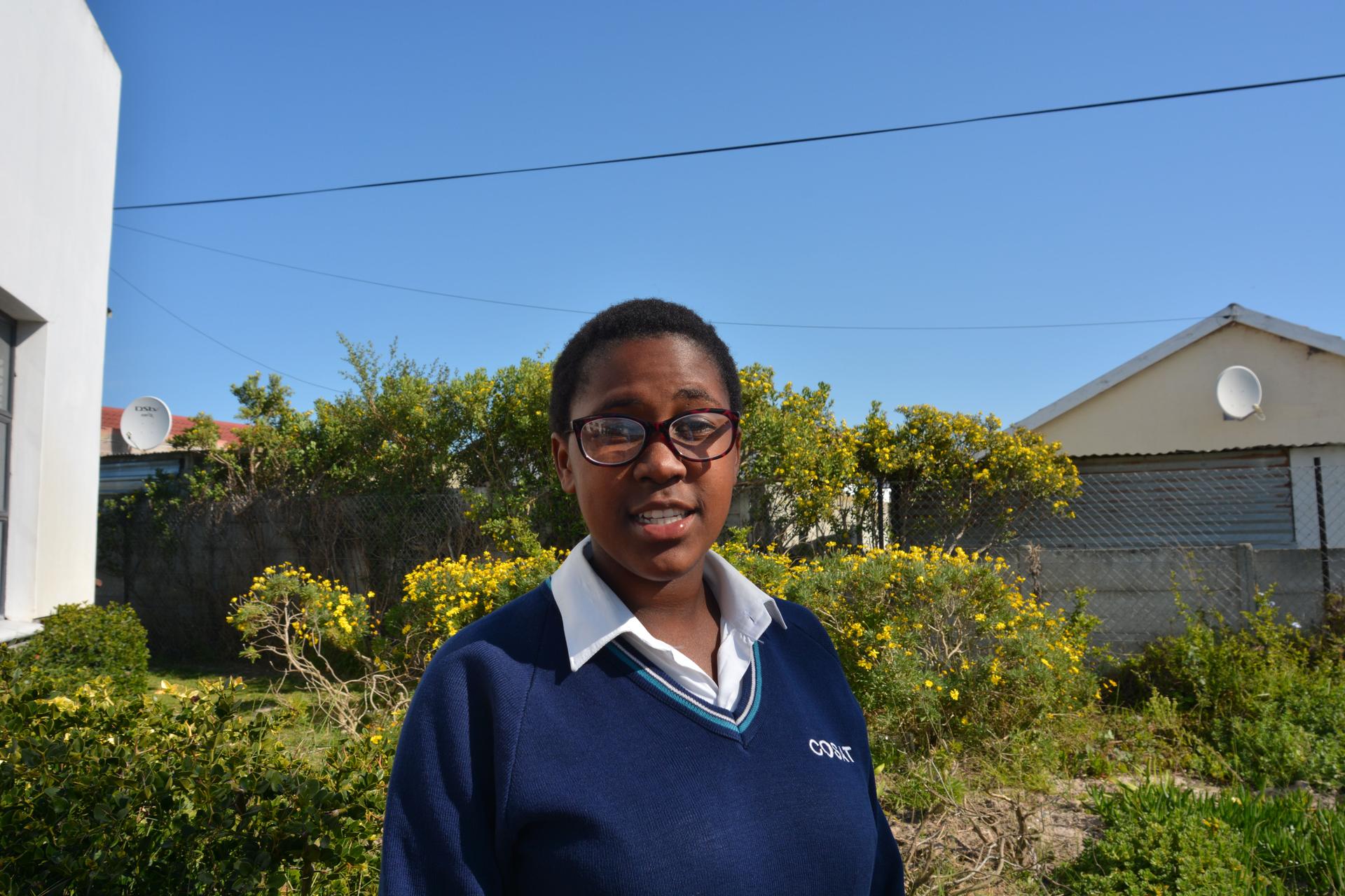 Teenager in a blue school uniform in front of shrubs at COSAT High School in South Africa.