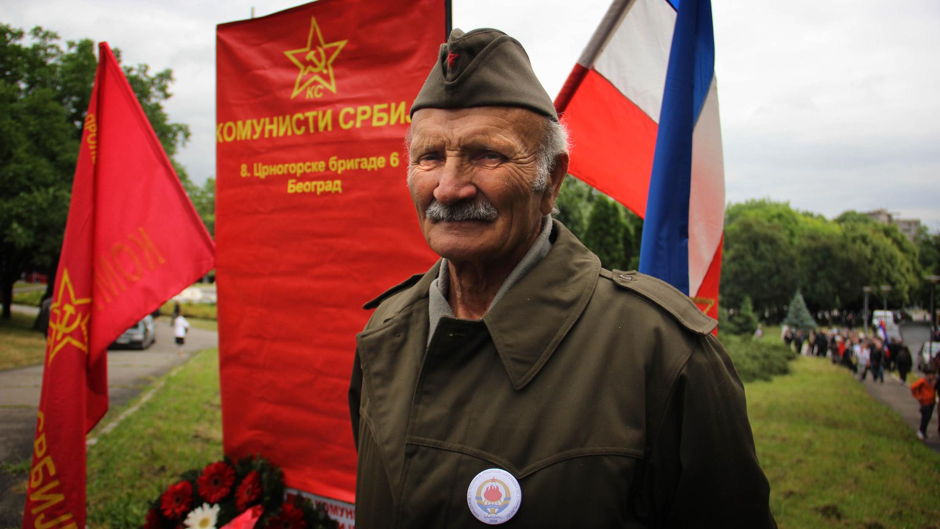 Man stands in front of a banner for the Serbian communists.