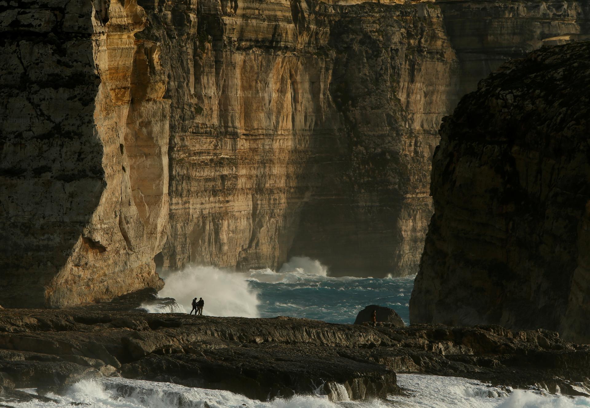 People watch as waves break on the shore next to Fungus Rock (R), close to where the structure known as the Azure Window collapsed