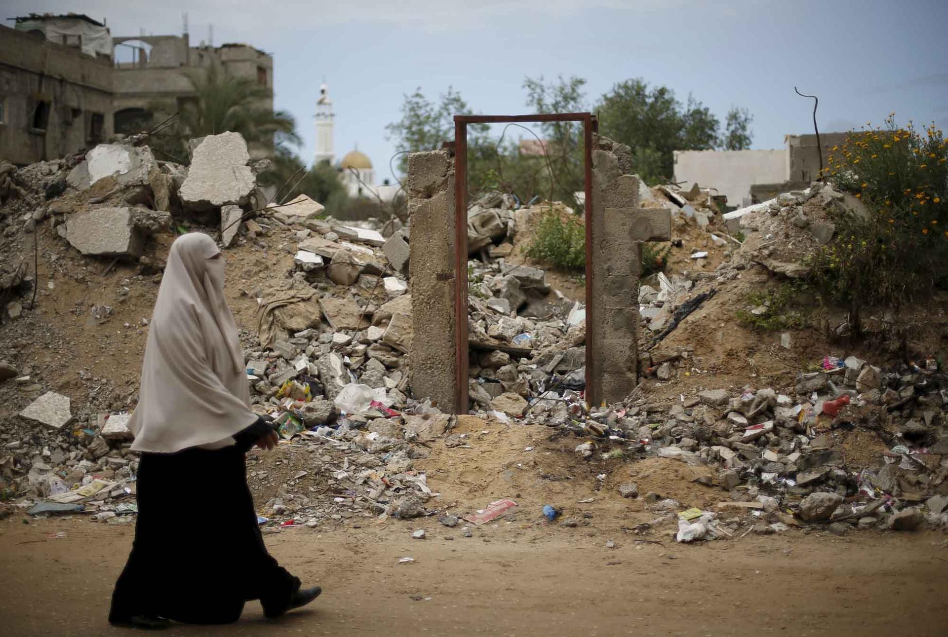 A Palestinian woman walks past the frame of a doorway of a destroyed house, on which British street artist Banksy painted an image of a goddess holding her head in her hand, after the door with the painted image was sold in the Gaza Strip.