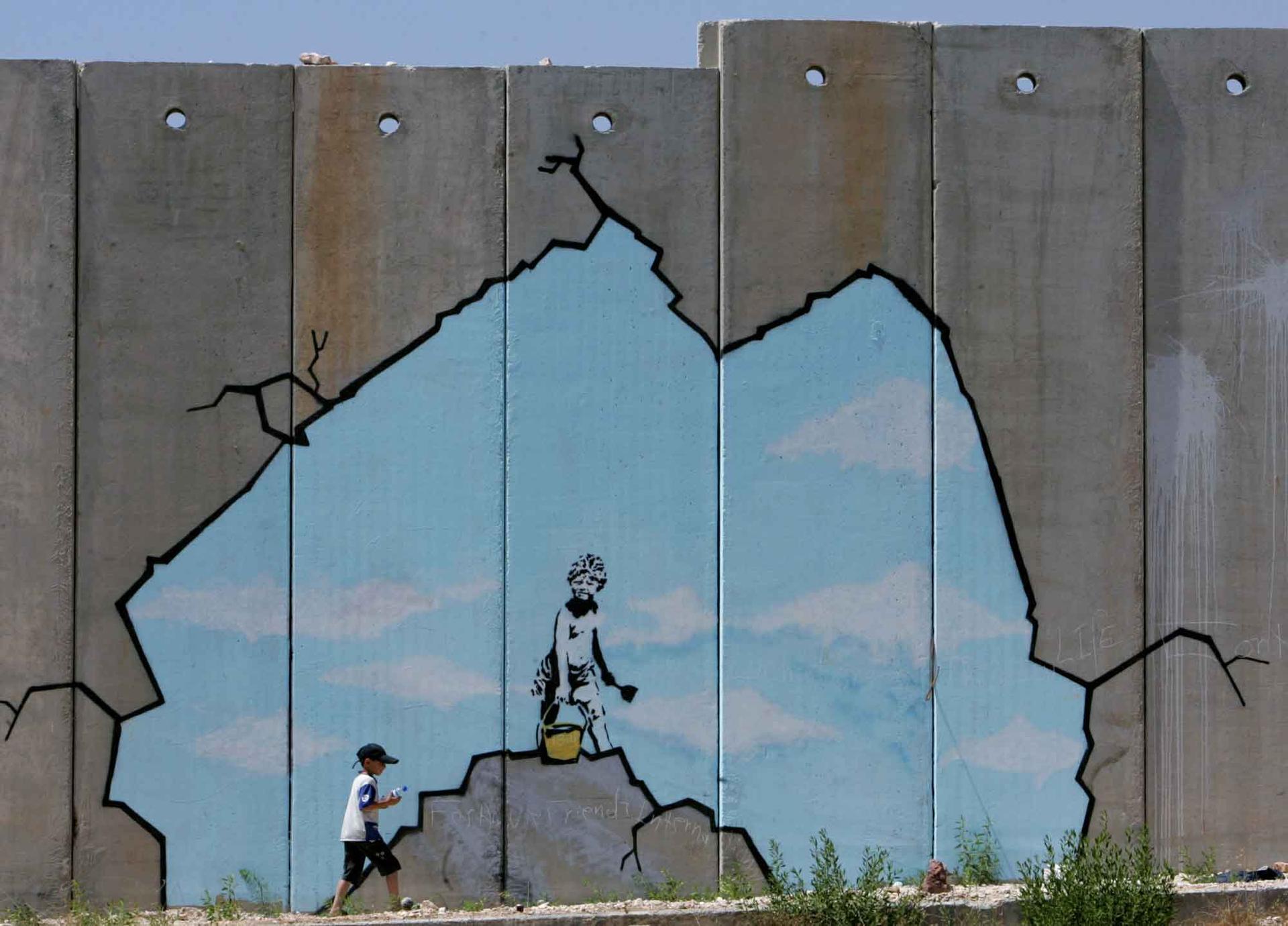 A Palestinian boy walks past a drawing by British graffiti artist Banksy, along part of the controversial Israeli barrier near the Kalandia checkpoint in the West Bank August 10, 2005.