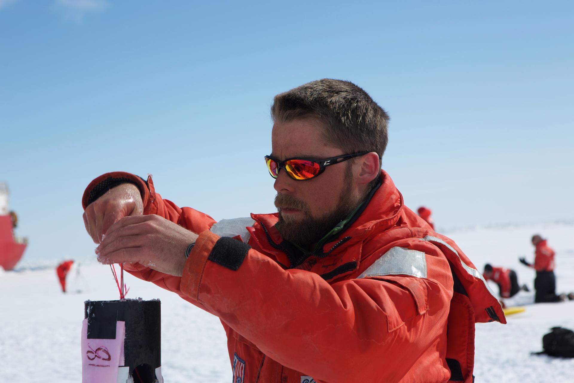 Geophysicist Chris Polashenski drops a pressure sensor into a plastic tube that he's using for his research into melt ponds that form on the Arctic ice every spring.