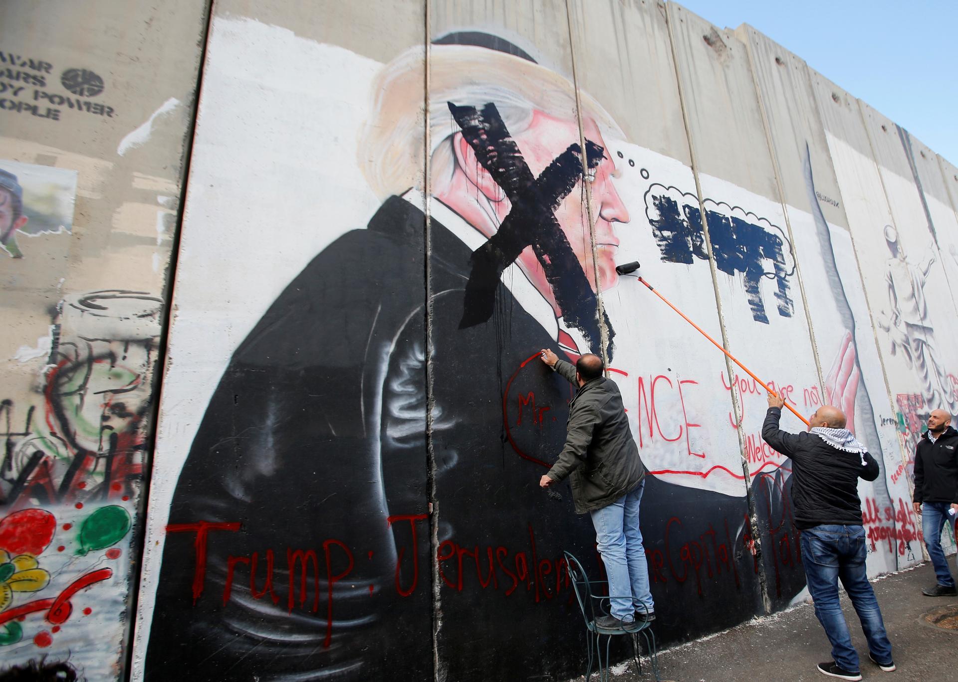 Men paint over a mural depicting US President Donald Trump painted on a part of the Israeli separation barrier, in the West Bank city of Bethlehem, Dec. 7, 2017.