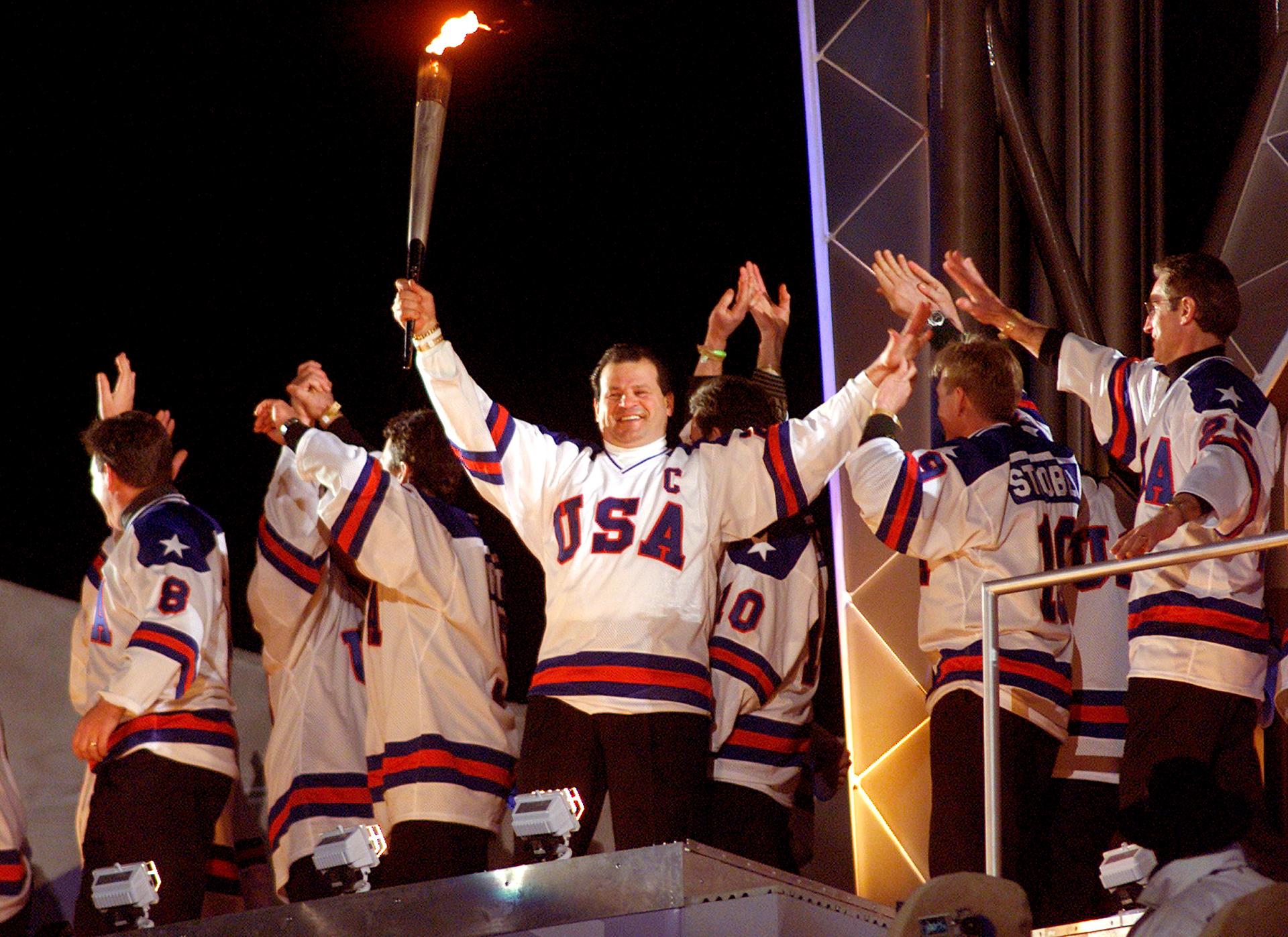 Members of the gold-medal winning 1980 US Olympic hockey team wave as their former team captain, Mike Eruzione, holds the Olympic torch during the opening ceremony of the Salt Lake 2002 Olympic Winter Games, February 8, 2002.