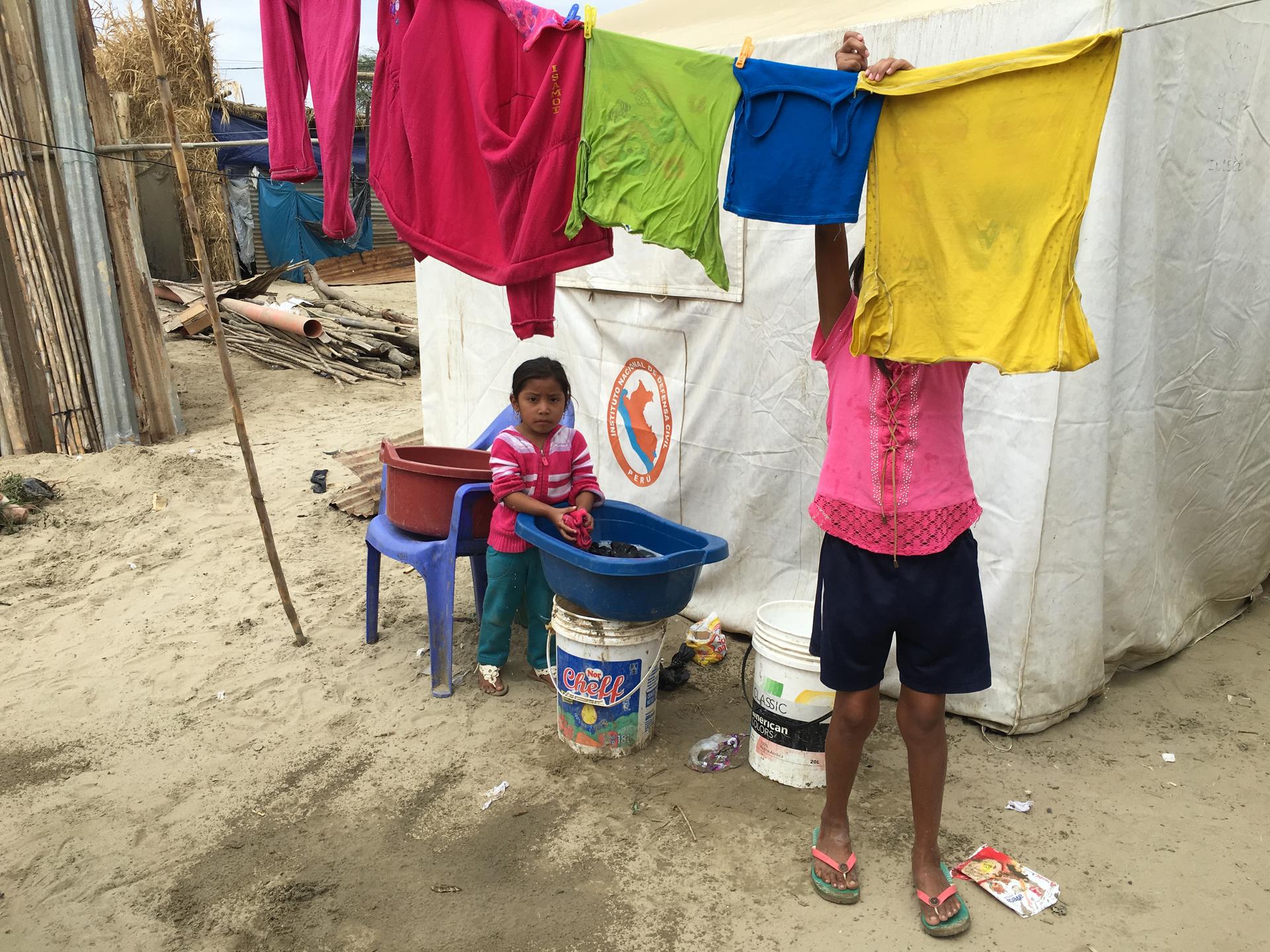 Children hang clothes to dry outside their tent on a clothsline in the village of Pedregal Chico.