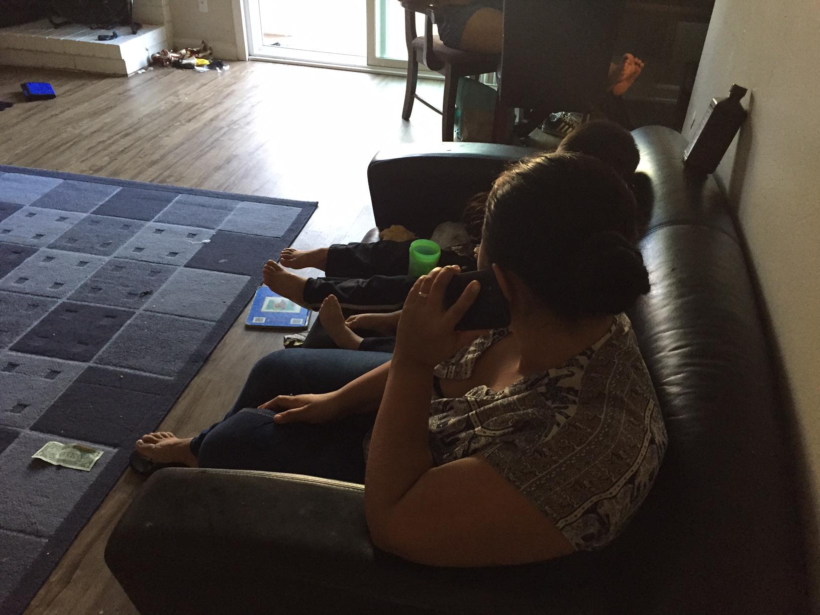 Woman on phone sitting on sofa, with kids next to her