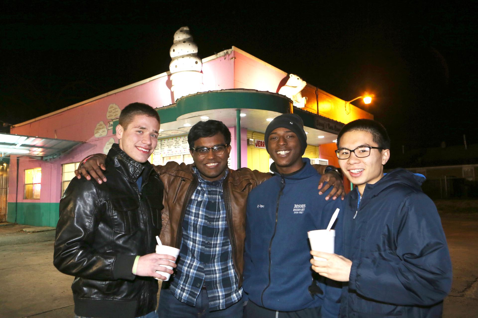 Four young men stand in front of ice cream shop, evening