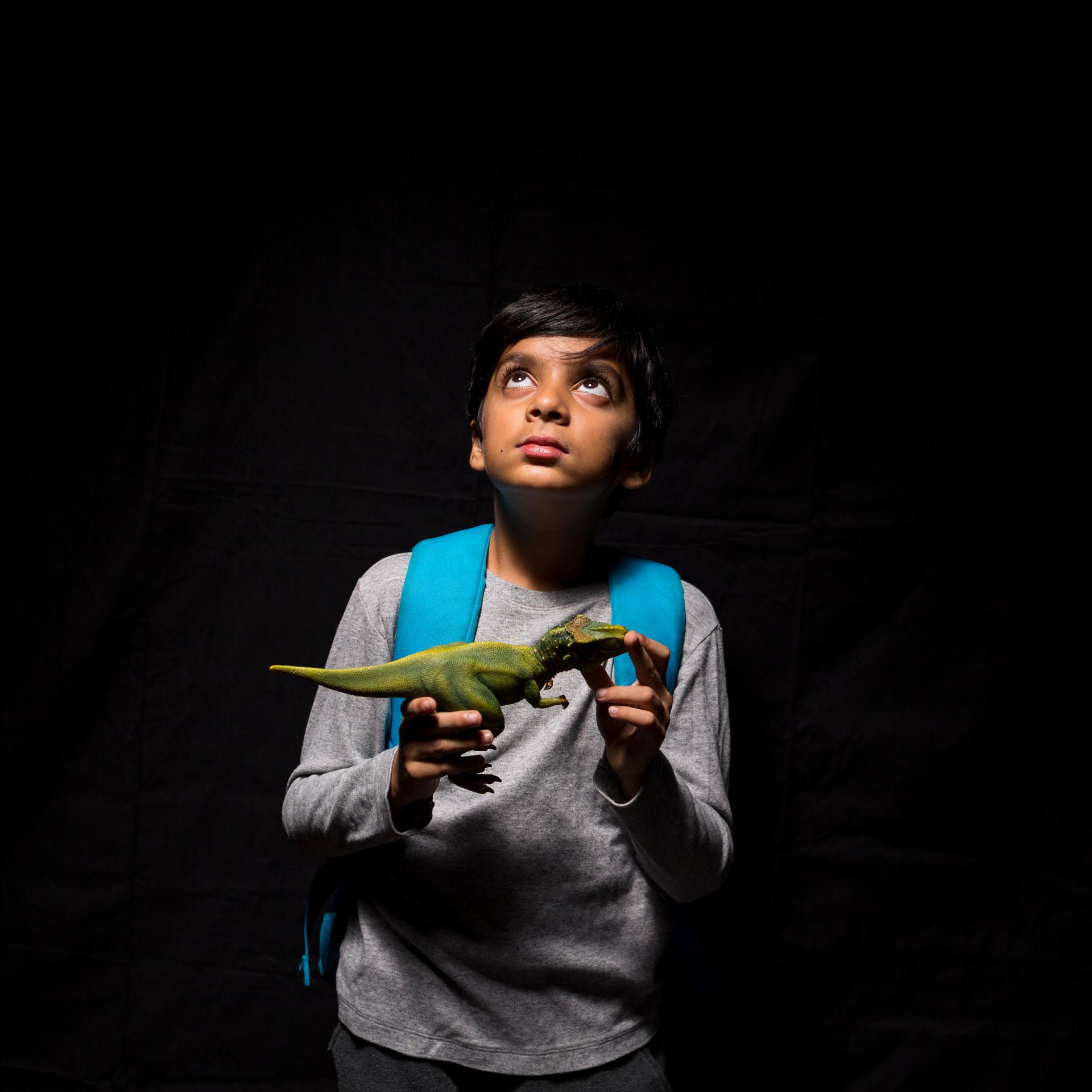Boy holding toy dinosaur looking up, against black background