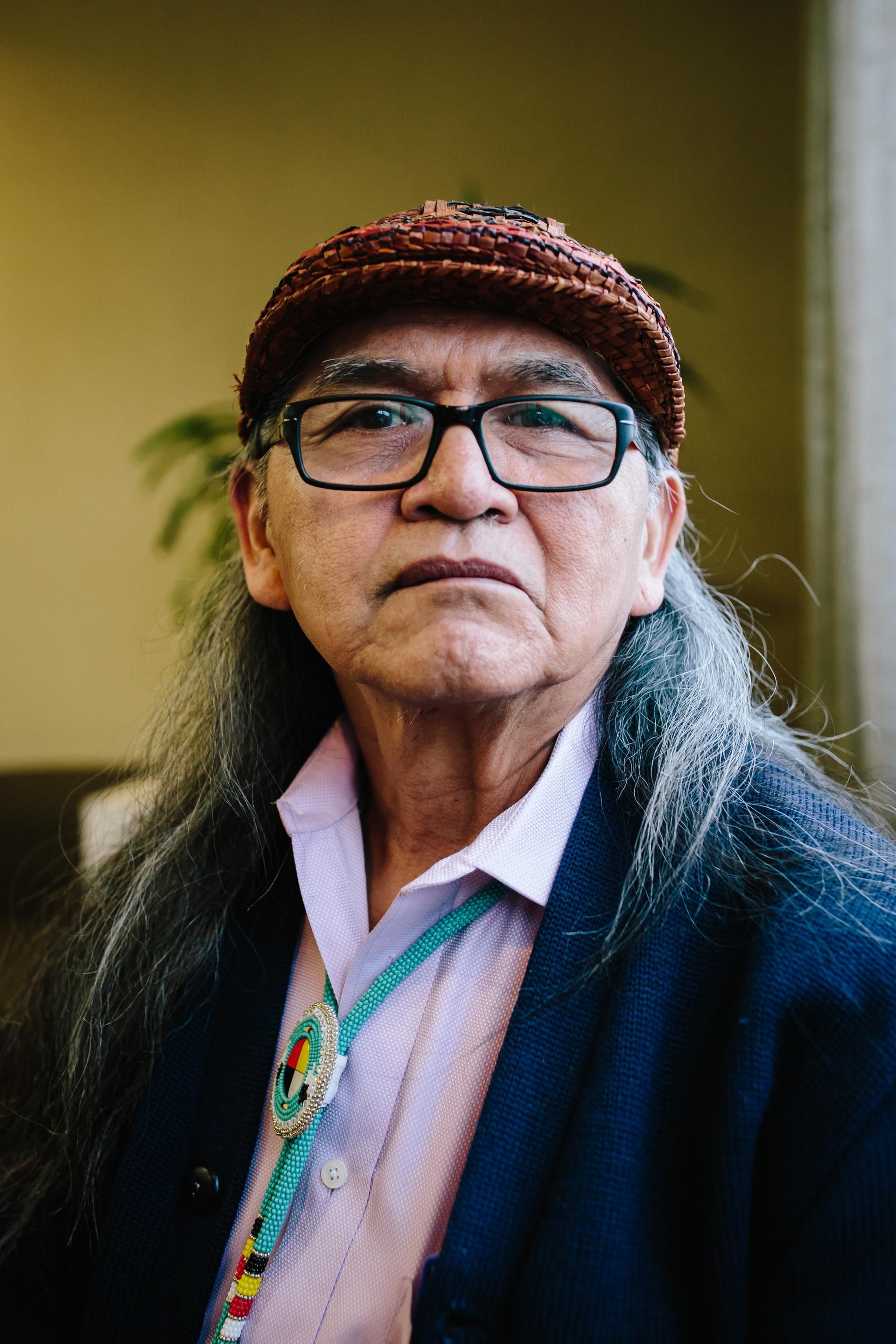 An older Indigenous man wearing hat looks towards the camera.