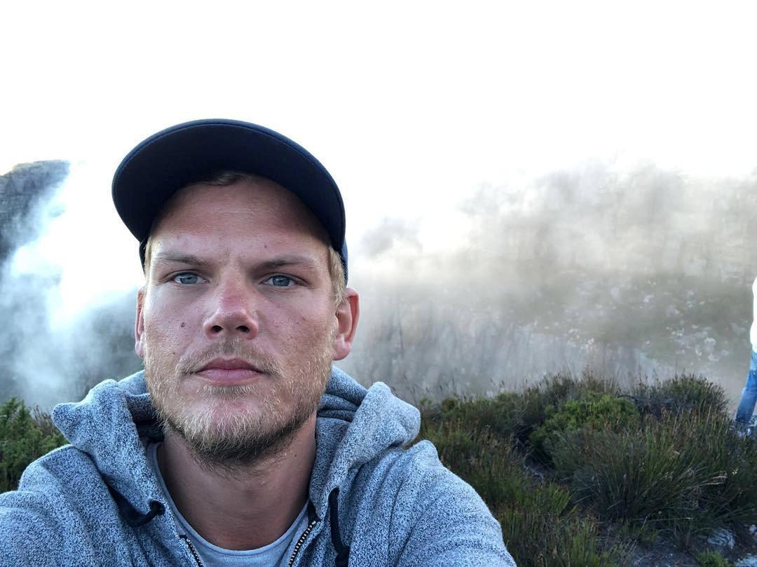 Swedish DJ Avicii wearing a hooded sweatshirt takes a selfie with Table Mountain in the background.