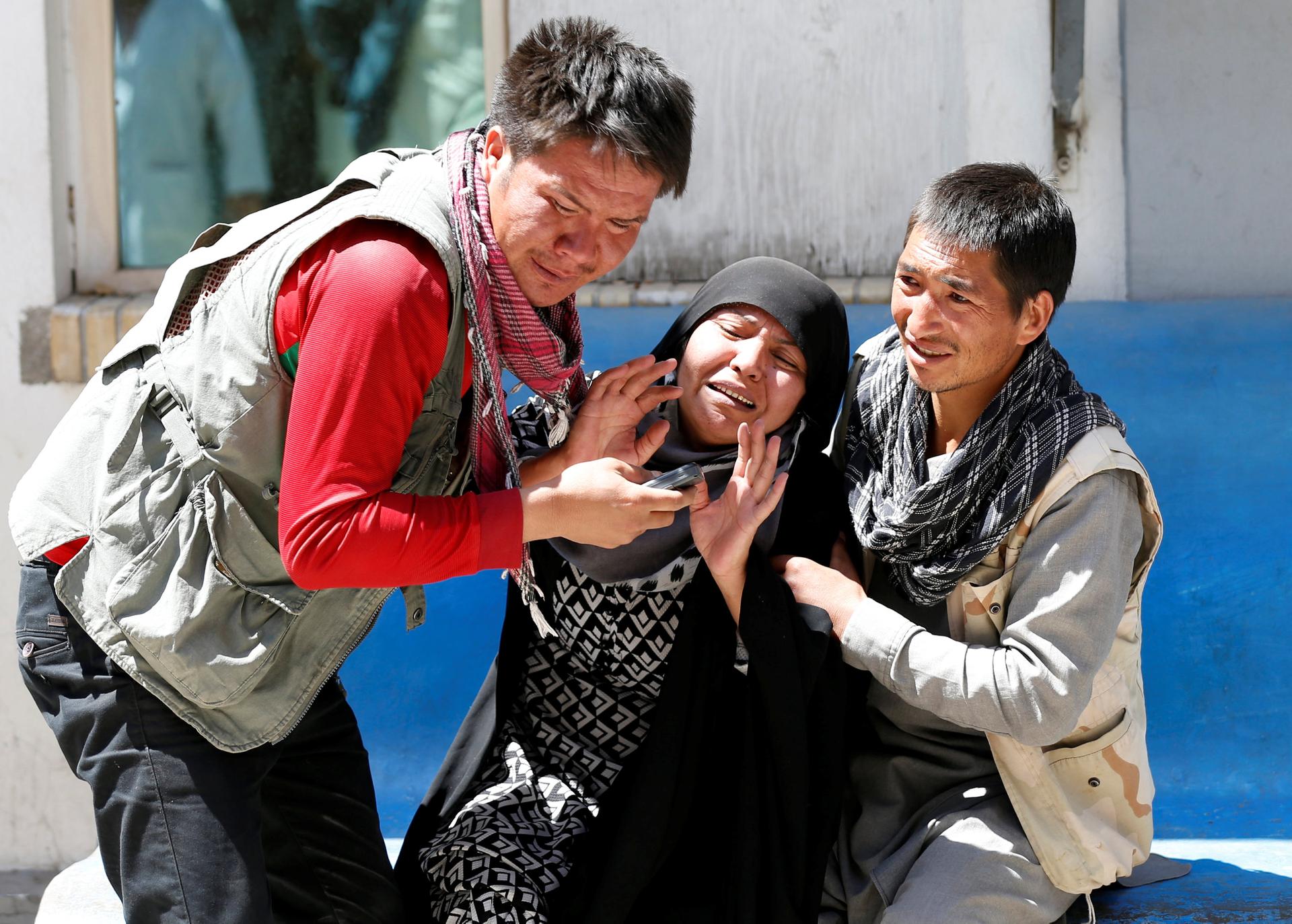 Two men hold of a greiving woman after a suicide attack in Kabul.