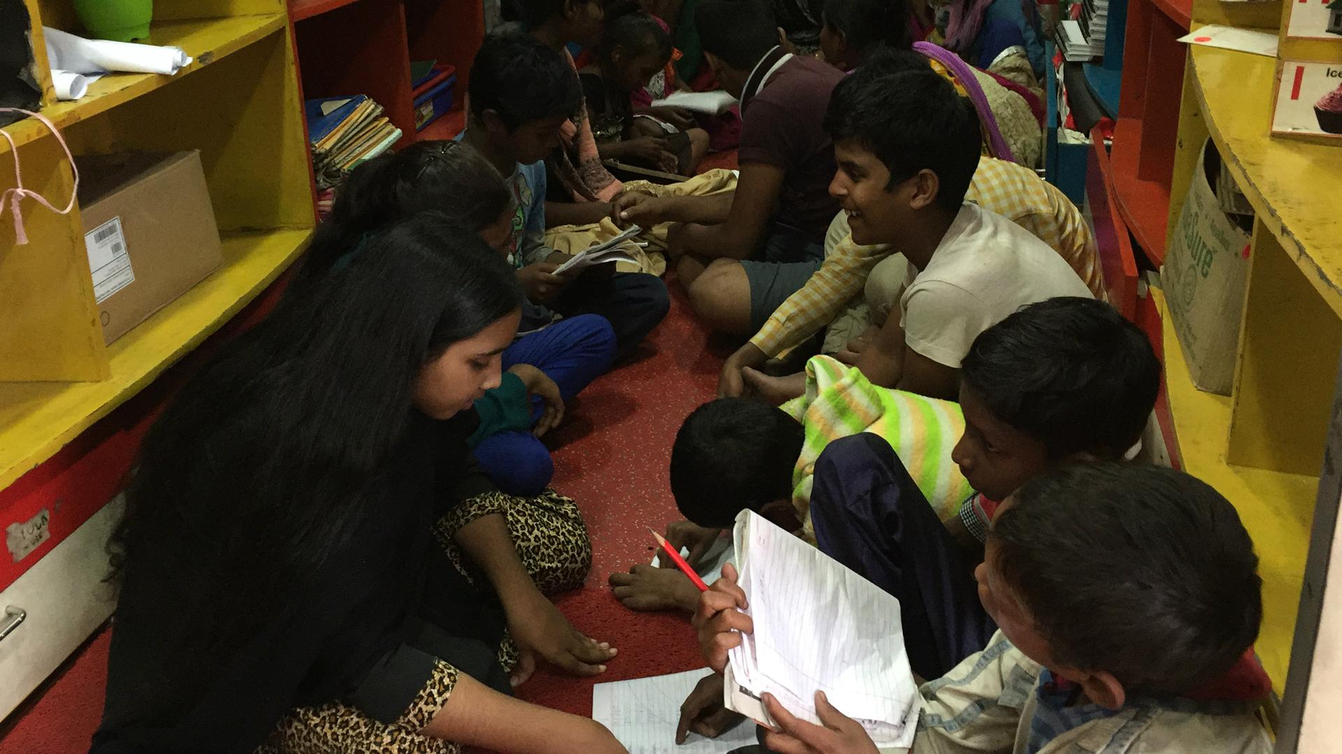 Children sit on the floor of s Save the Children mobile learning center tutoring each other.