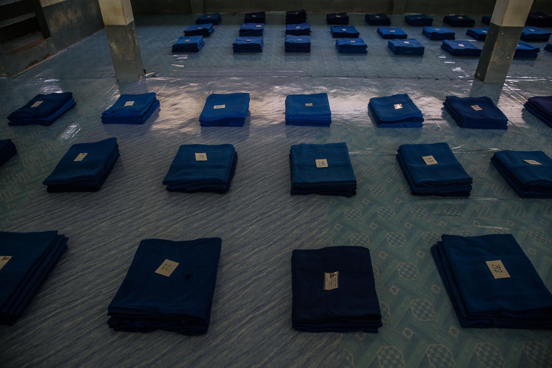 Blue blankets are folded in tidy rows across a carpet, with a number placed atop each one.
