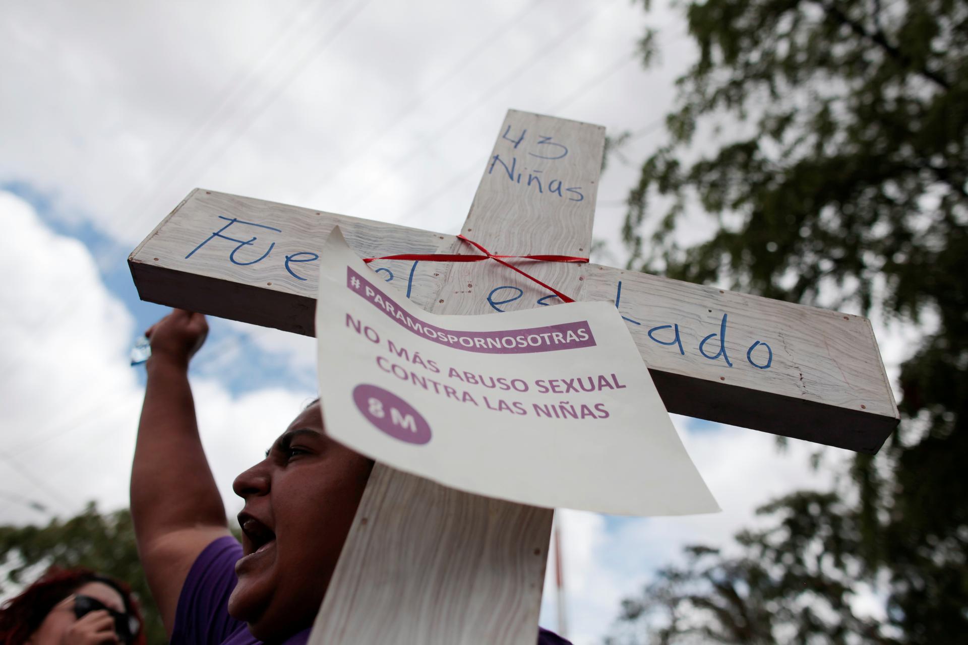 An activist holds a cross with a sign that reads 
