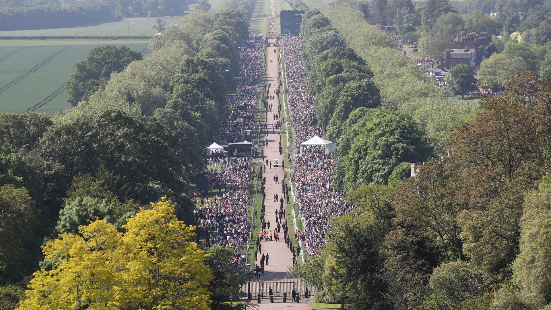 An aerial photo shows a road lined with thousands of people. To the right, is a stone castle.