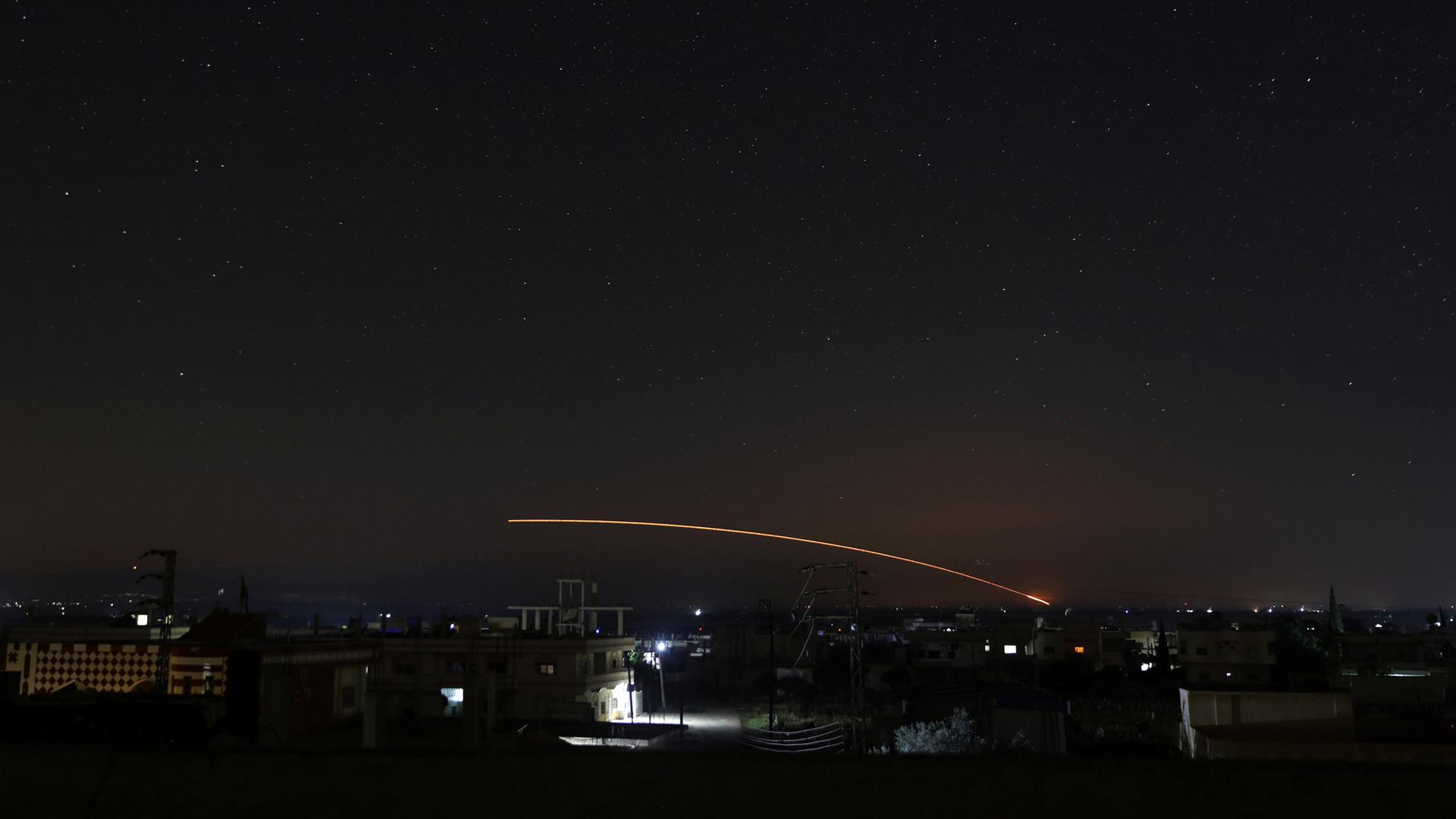 Missile fire is seen in a yellow streak across the night sky over Daraa, Syria.