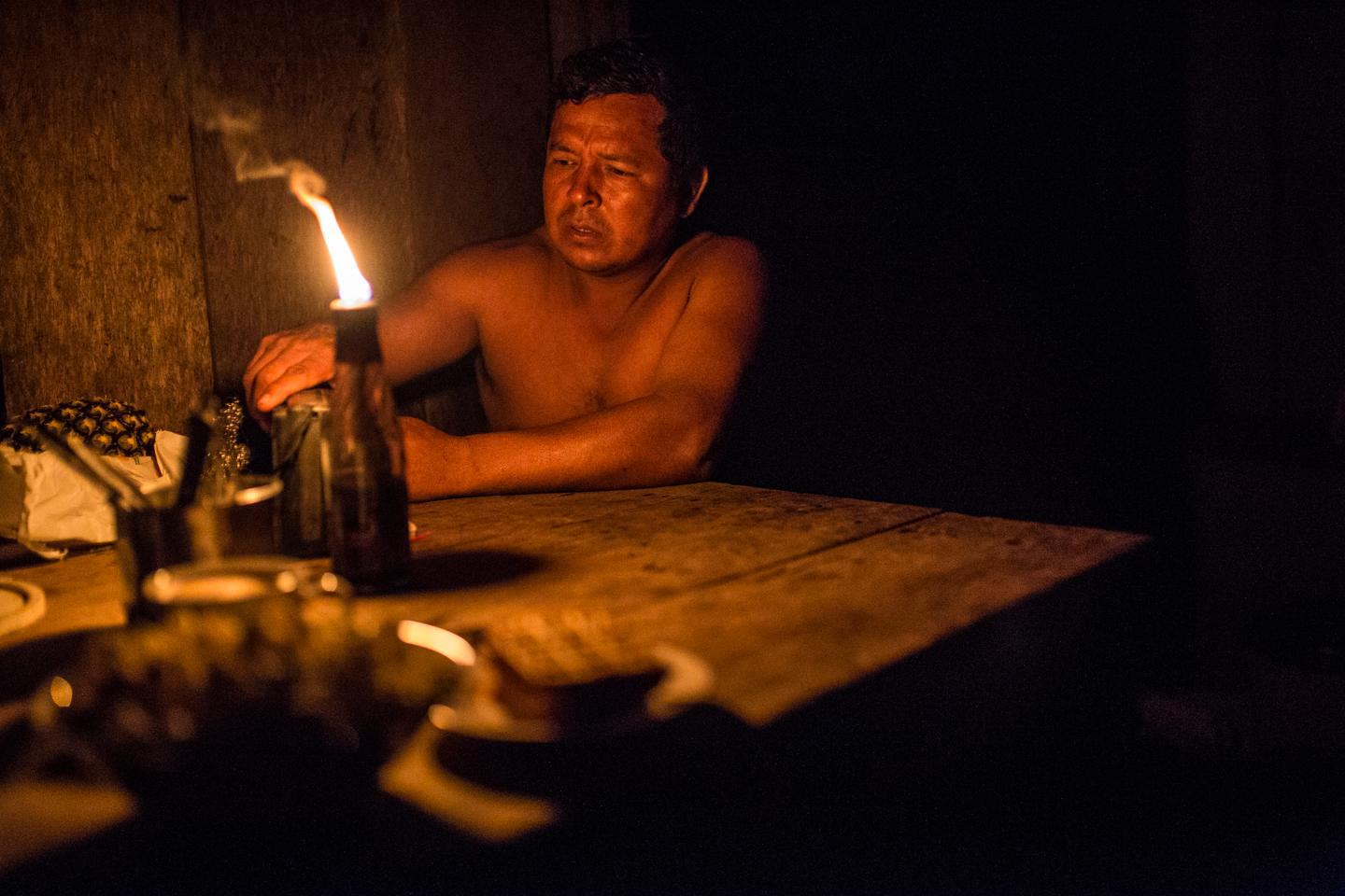A man sits in a shack lighted by a candle.