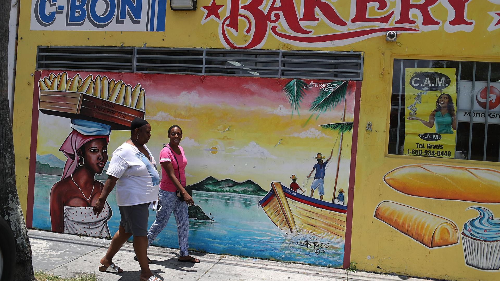Women walk past a mural in the Little Haiti neighborhood in Miami, May 17, 2017.