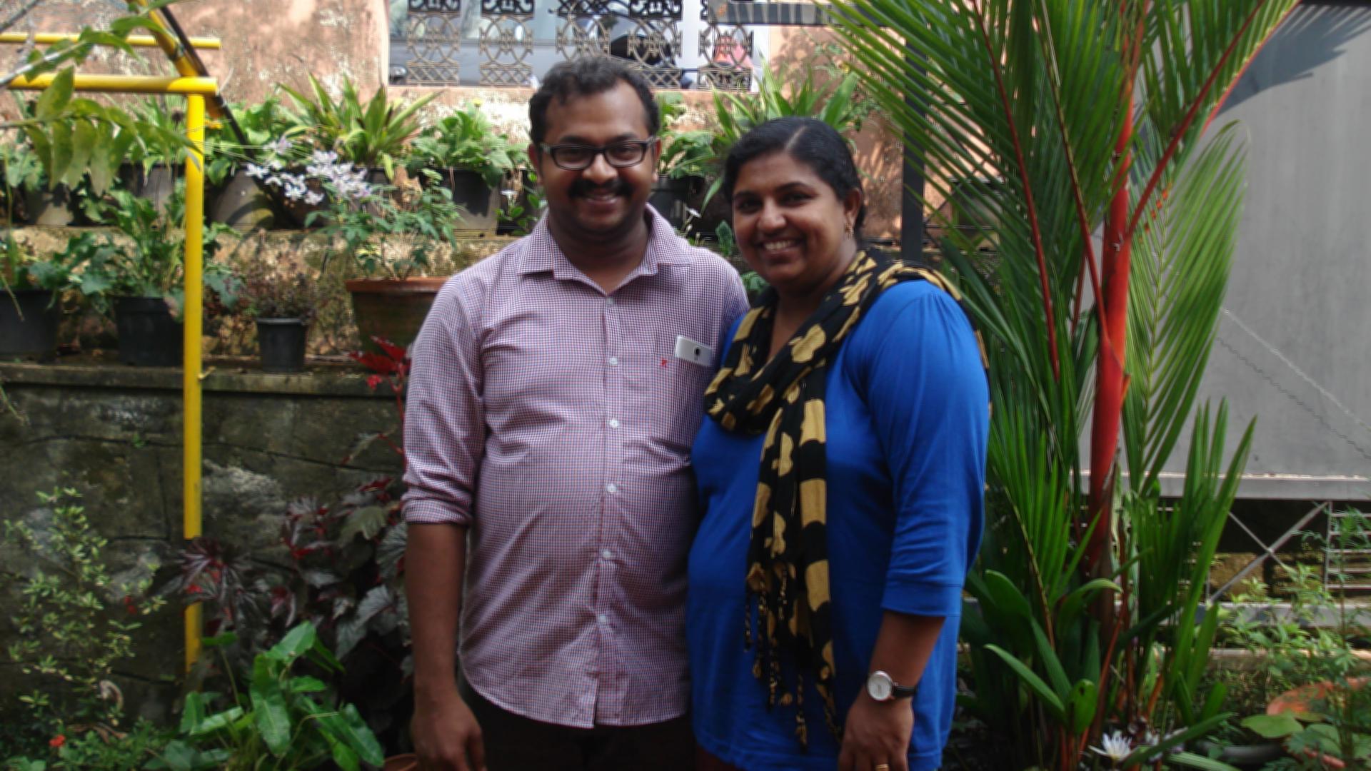 Sujitha (right) and her husband Manu (left) stand in the center of the frame in a portrait photograph.