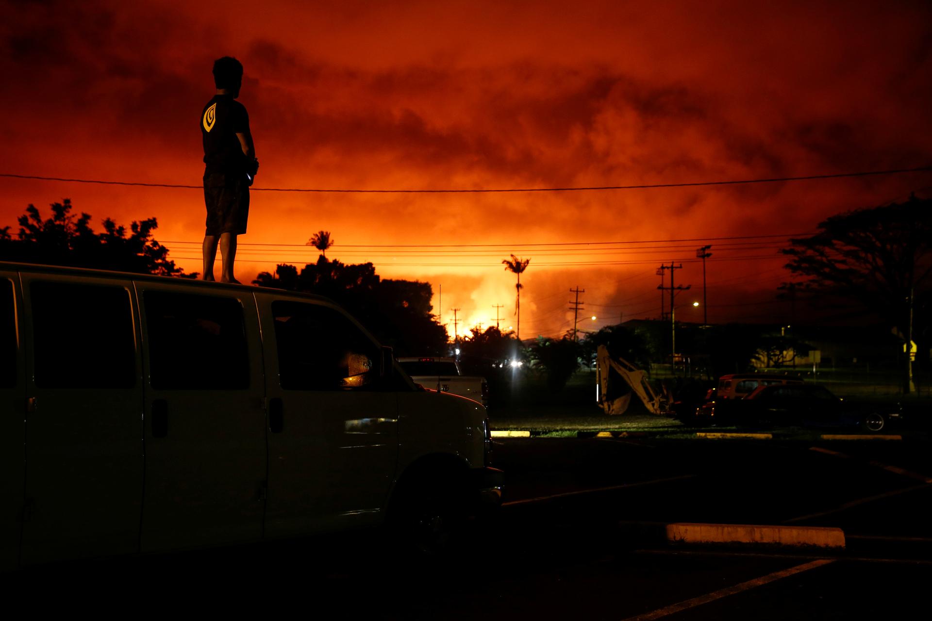 Darryl Sumiki, 52, of Hilo, stands atop a car and watches as lava lights up the sky in bright red above Pahoa during ongoing eruptions of the Kilauea Volcano in Hawaii.
