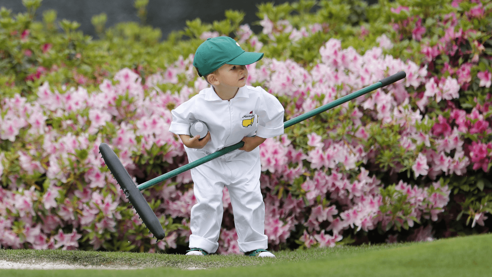 a little boy is dressed in a white gown at a golf event