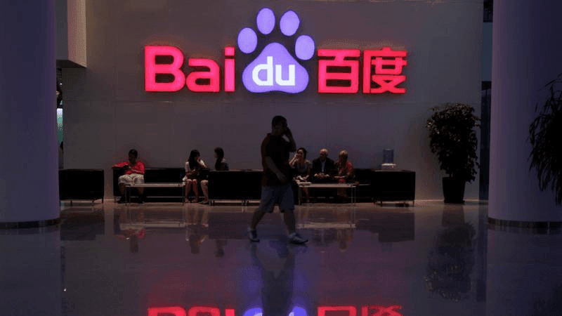 An employee uses his mobile phone as he walks past the company logo of Baidu at its headquarters in Beijing, Aug. 5, 2010. 