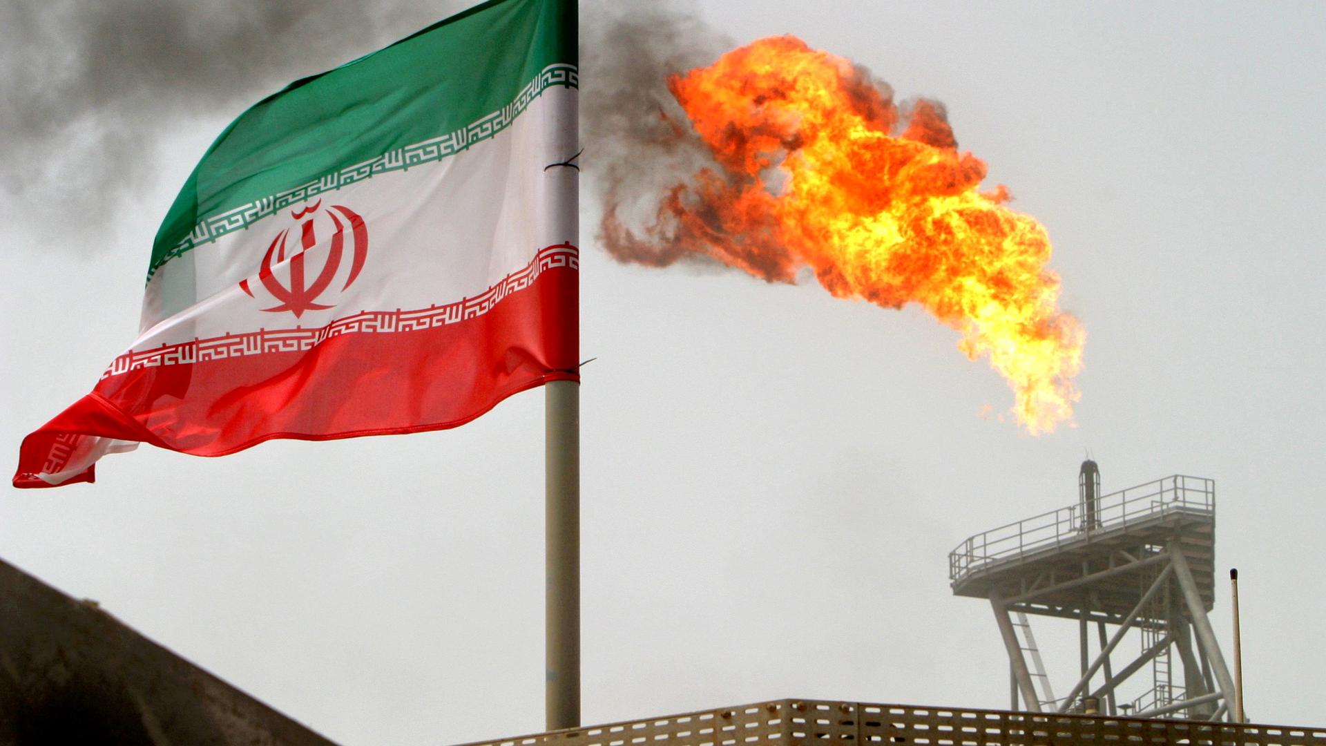 A gas flare is seen in the background with the Iranian flag flying in the wind in the foreground.