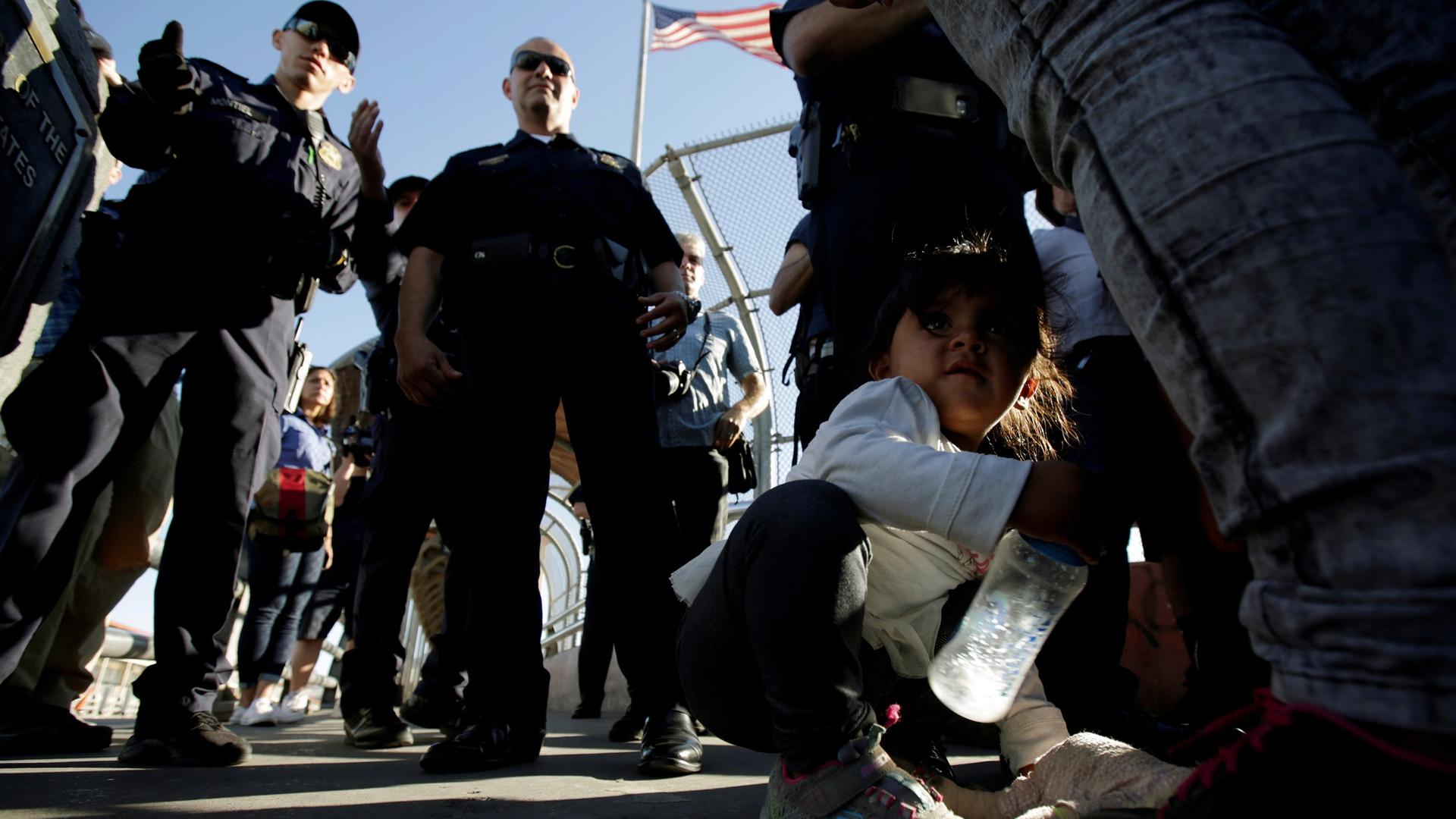 A you migrant girl crouches next to her family as they listen to officers of the US Customs and Border Protection before entering the United States to apply for asylum.