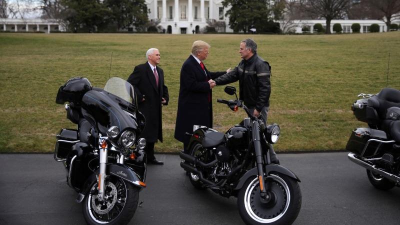 US President Donald Trump shakes hands with Matthew Levatich, CEO of Harley-Davidson, accompanied by Vice President Mike Pence in a picture with two motorcycles in the foreground and the White House in the background.