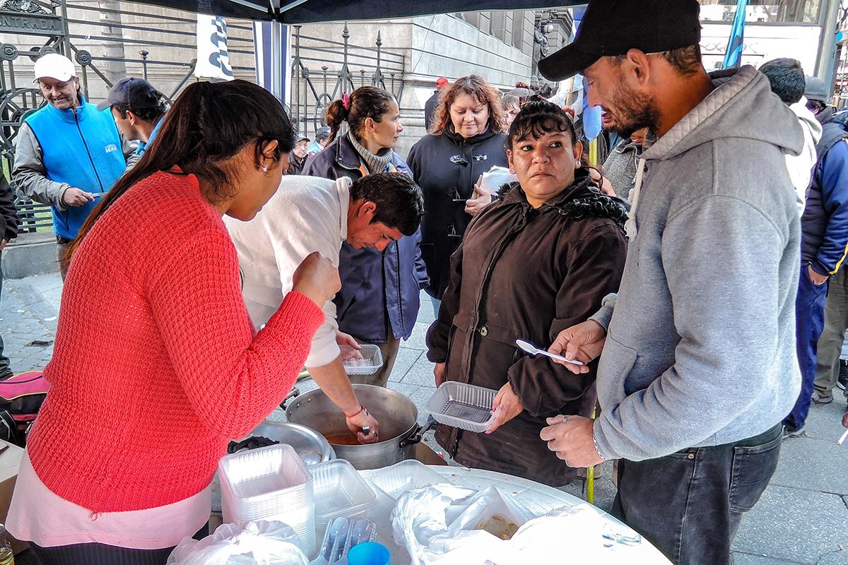 Paola Sarabia, in brown coat, offers warm stew to people lined up in front of Argentina’s congressional building. Sarabia hopes lawmakers will see how many Argentines rely on food banks.