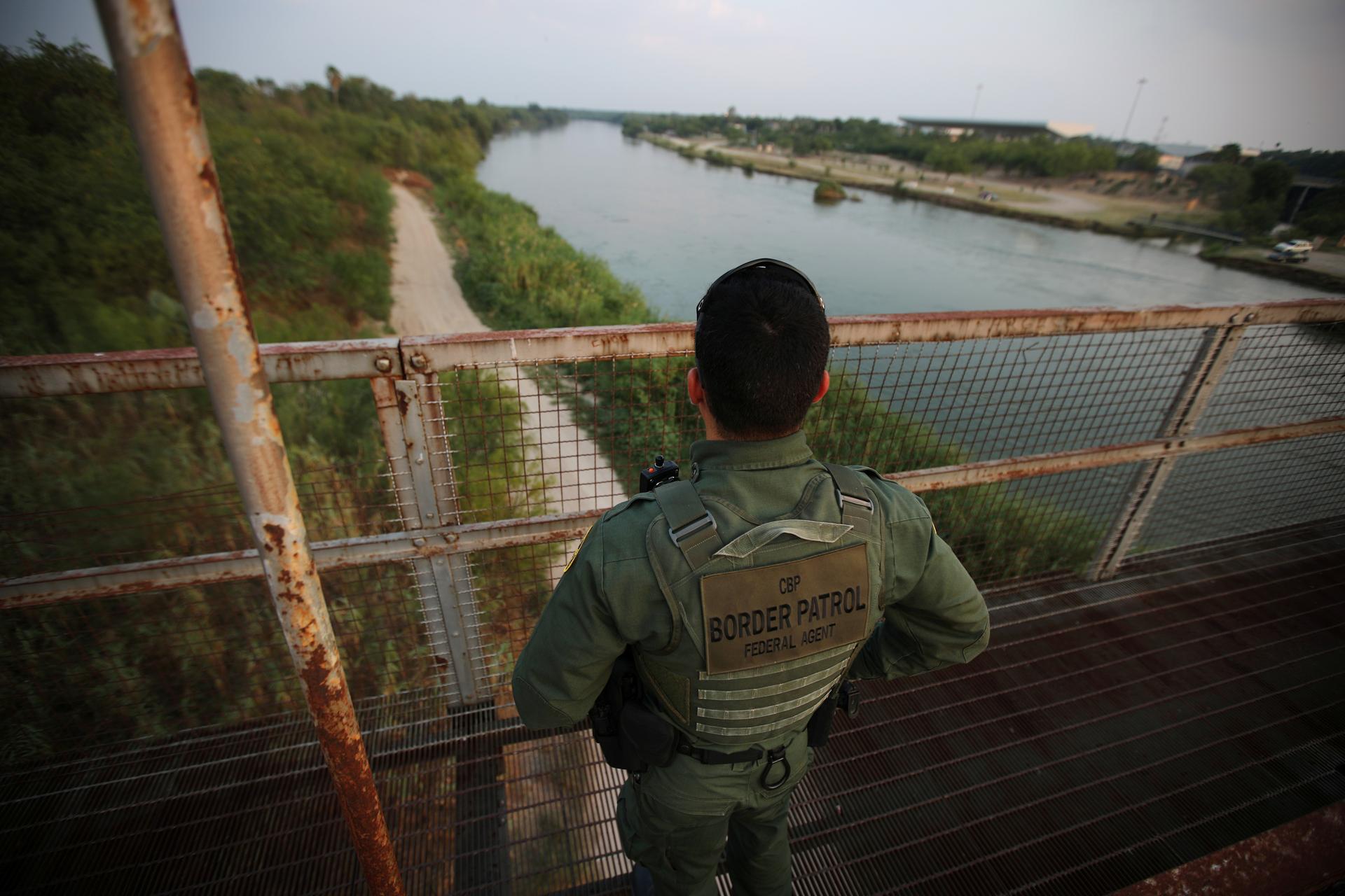 Agent in uniform stands on bridge looking over green river