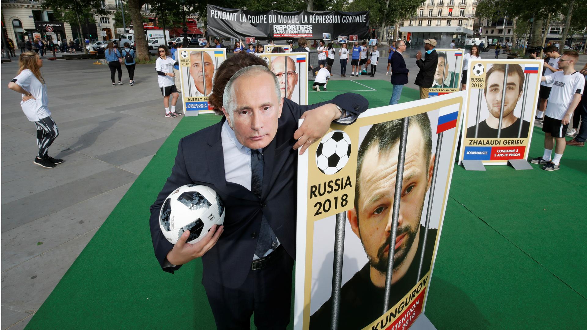 An activist with Reporter Without Borders, wearing a mask depicting Russian President Vladimir Putin, stands next to a giant portrait of imprisoned Russian journalist Alexei Kungurov on the Place de la Republique