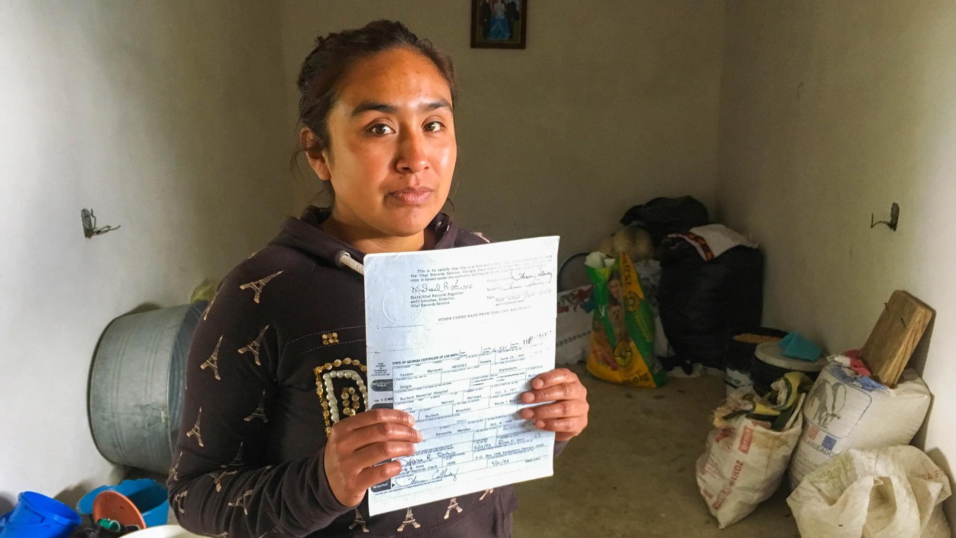 Young woman in plain room, dirt floor, holding birth certificate
