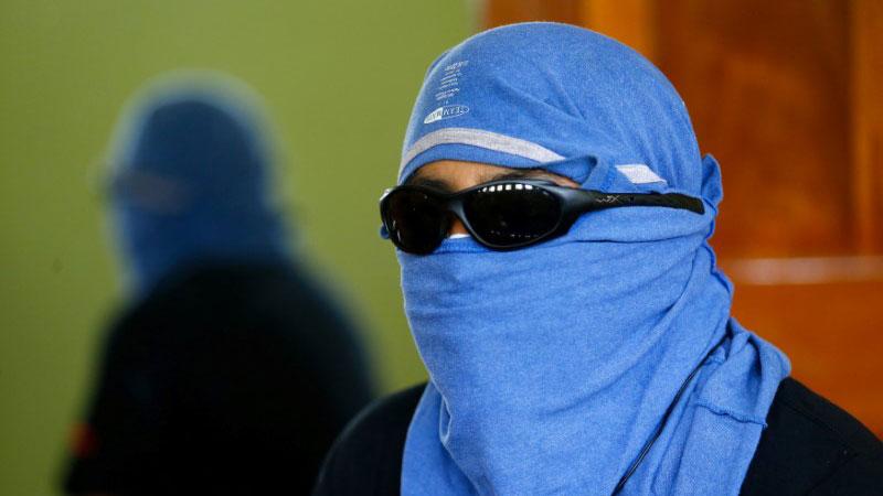 A man wearing sunglasses and a blue T-shirt around his head speaks