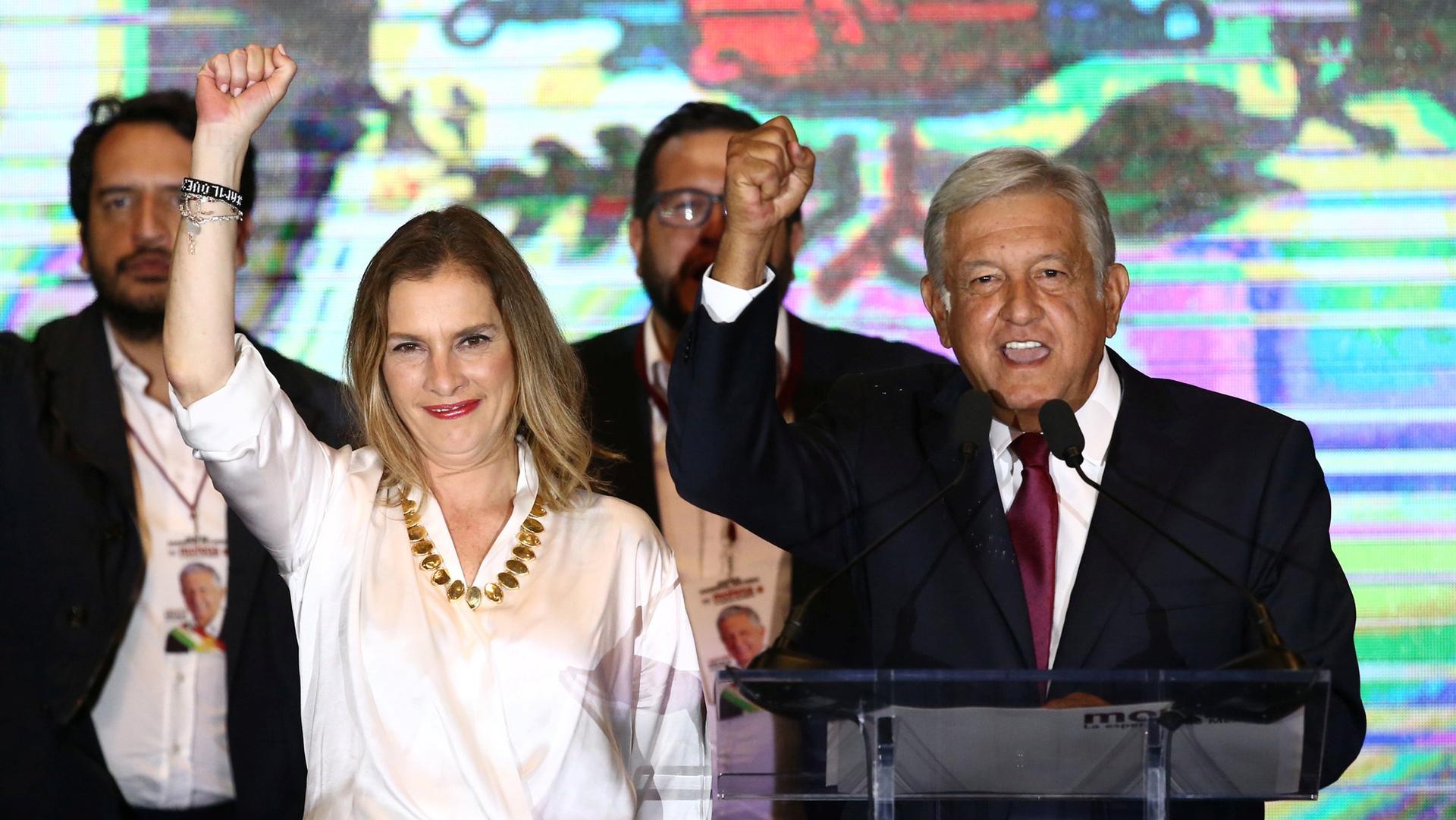 Andrés Manuel López Obrador and his wife Beatriz Gutierrez Muller raise their clenched hands on a stage in Mexico City.