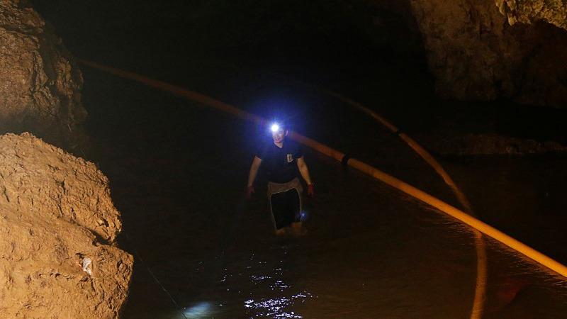 A diver walks in Tham Luang cave complex wearing waders and a headlamp.